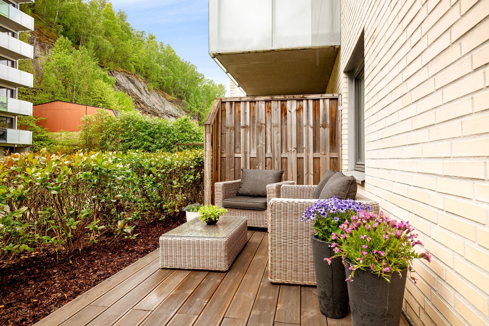 Terrassen har terrassebord på gulv, levegger av treverk i begge ender og hekk i front. Galleribilde