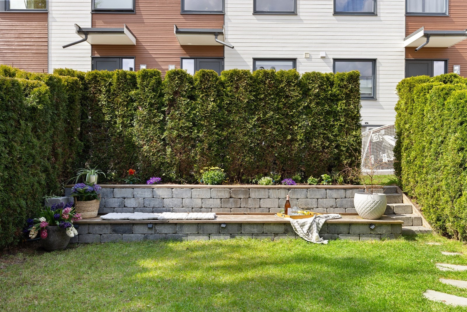 Pent opparbeidet uteplass med blomsterbed, sittebenk i naturstein med integrert belysning, og mulighet til å dekorere med planter og lykter. Galleribilde