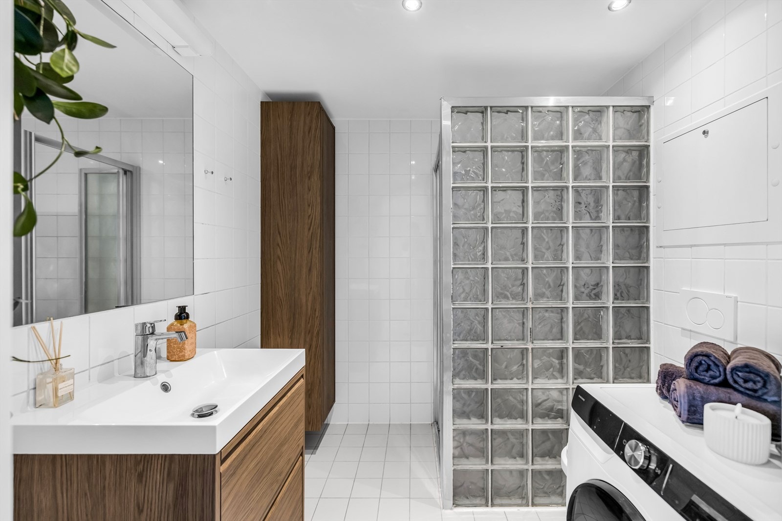 Badet er innredet med vegghengt toalett, servant med tilhørende innredning, speil med belysning samt dusjhjørne med skyvbar glassdør og dekorativ glassbyggerstein. Galleribilde