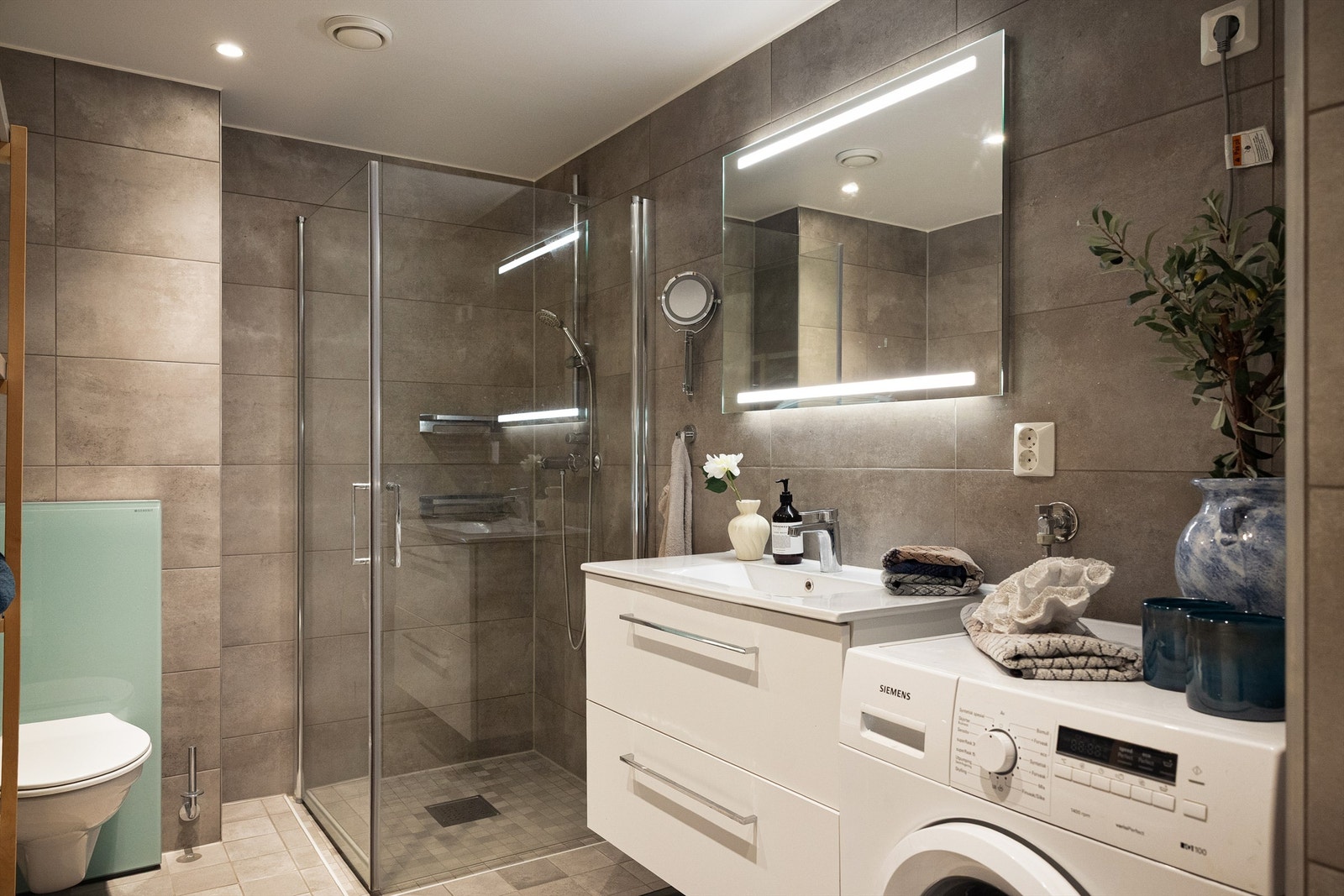 Badet holder en moderne standard med flislagte overflater, vannbåren gulvvarme og praktisk opplegg for vaskemaskin. Galleribilde