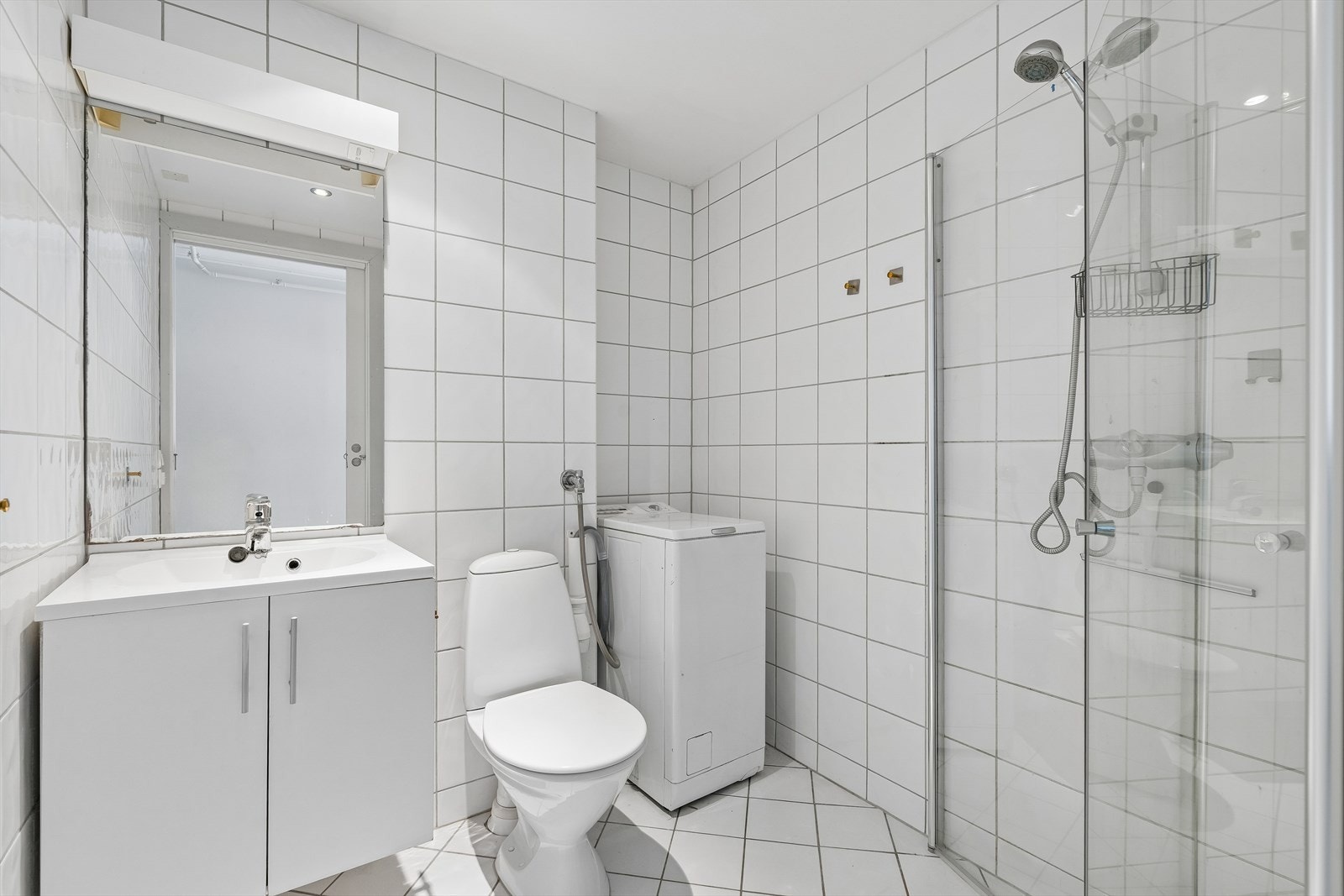 Flislagt bad med varmekabler i gulvet, dusjhjørne med glassdører og opplegg for vaskemaskin. Galleribilde