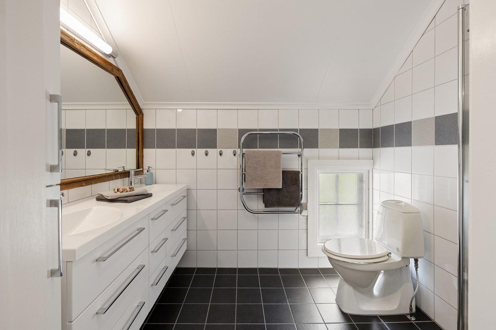 Badet har flislagt gulv med gulvvarme og et gulvmontert toalett. Galleribilde