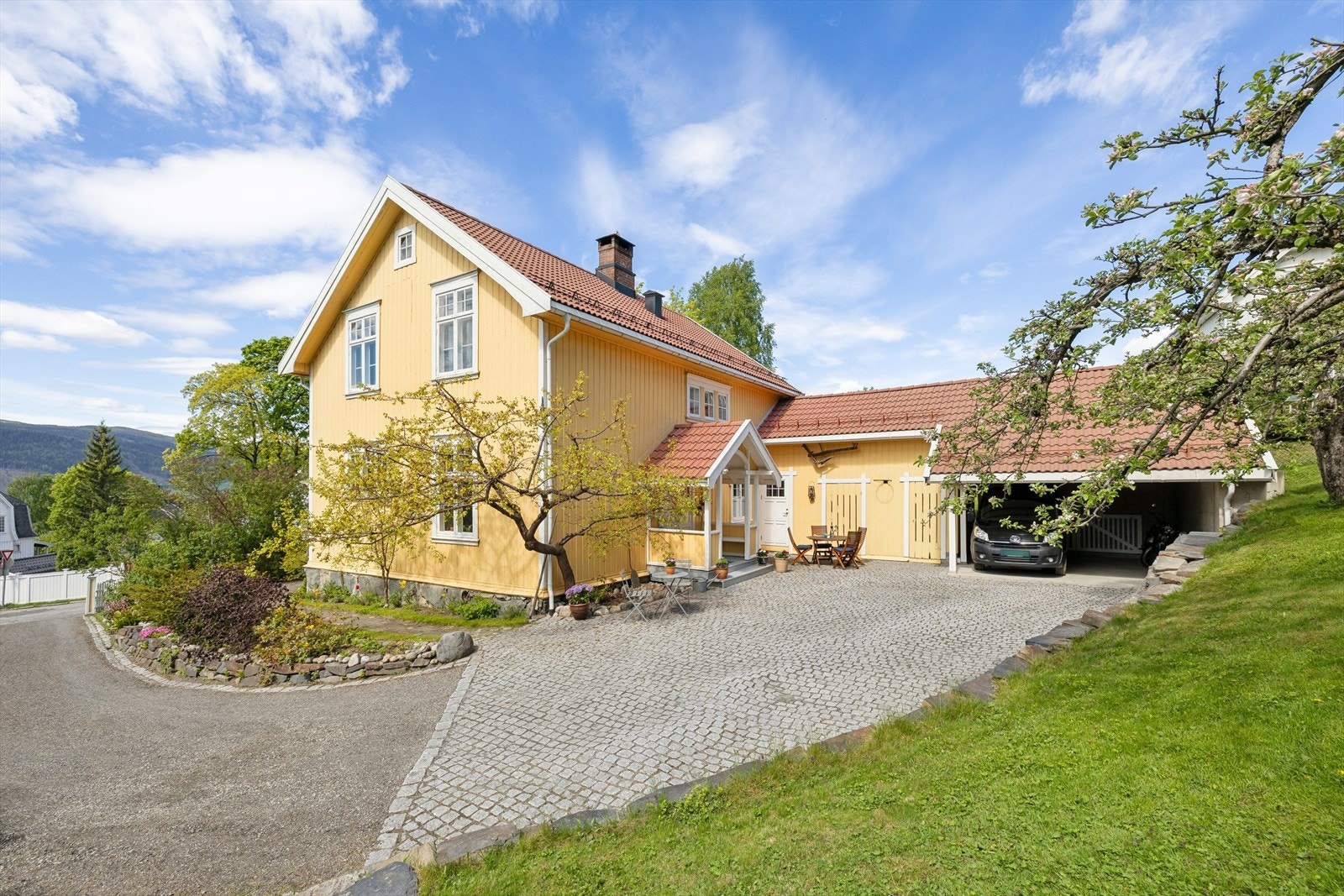 Adkomst til eiendommen via portstolper og gruset vei opp til en romslig, steinlagt gårdsplass. Galleribilde