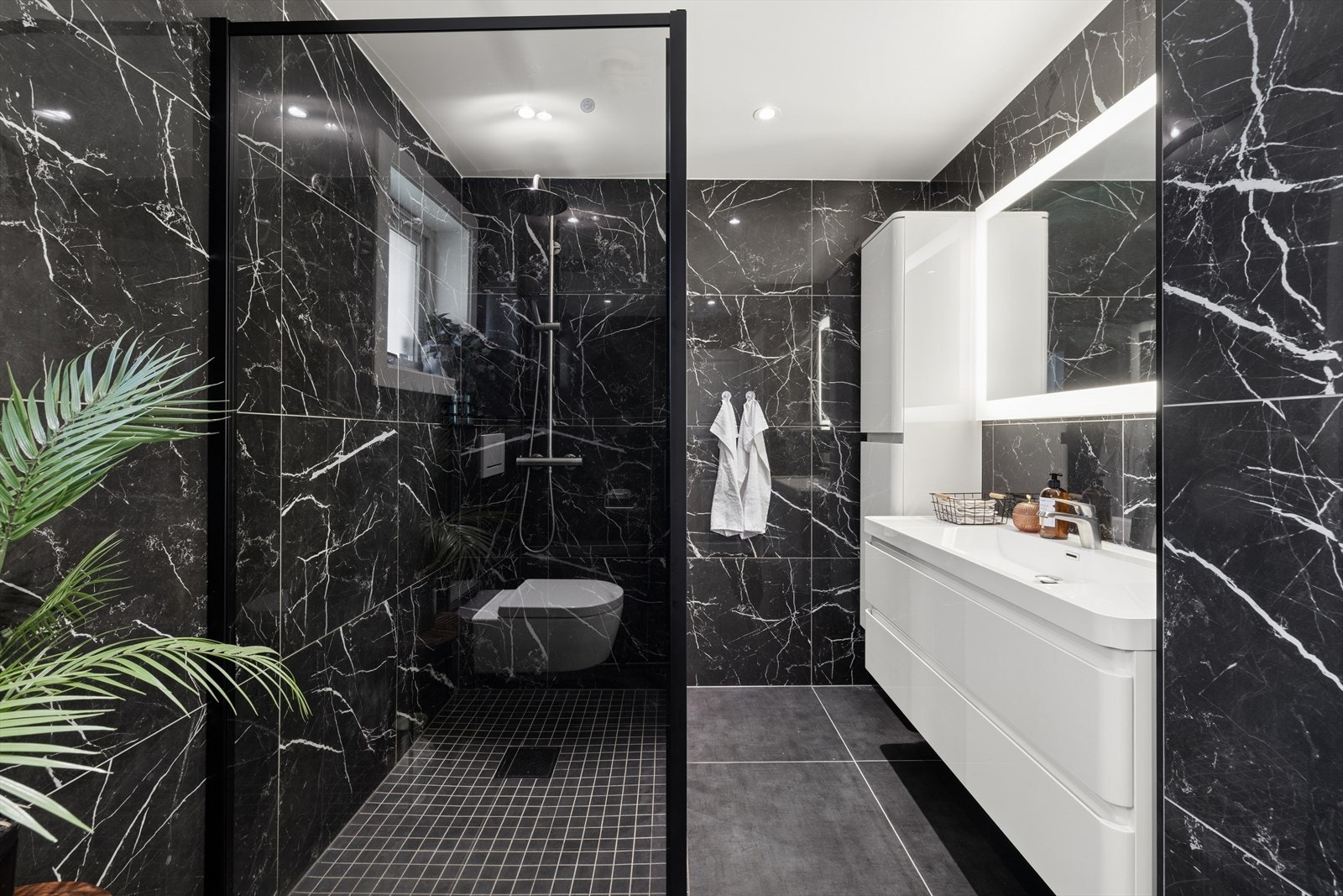 Badet innredet med dusj, servant og veggfestet klosett. Baderomsinnredning med benke- og veggskap med glatte fronter, samt speil over servant. Galleribilde