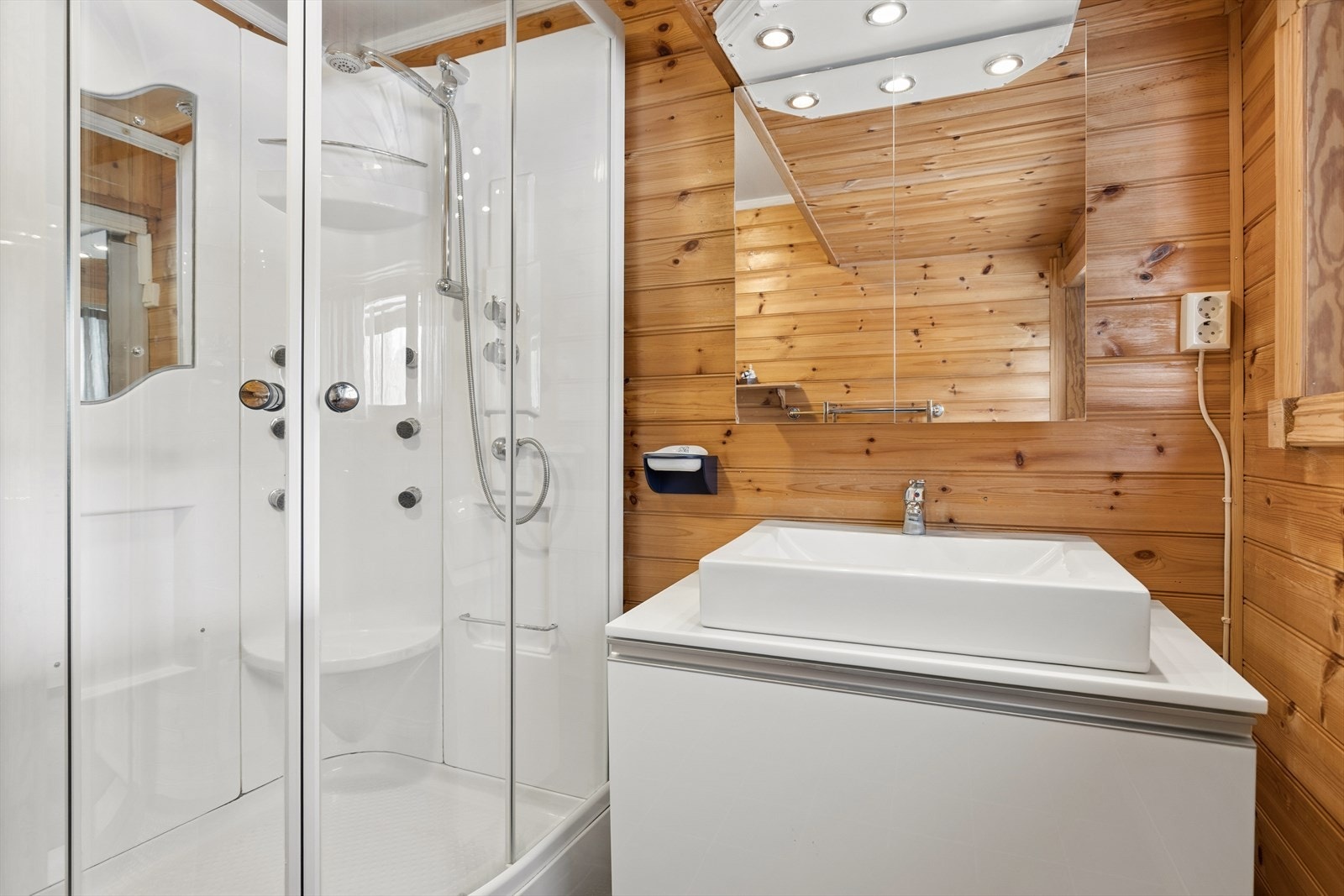 Badet er utstyrt med dusjkabinett, servant med underskap og overskap med belysning. Galleribilde