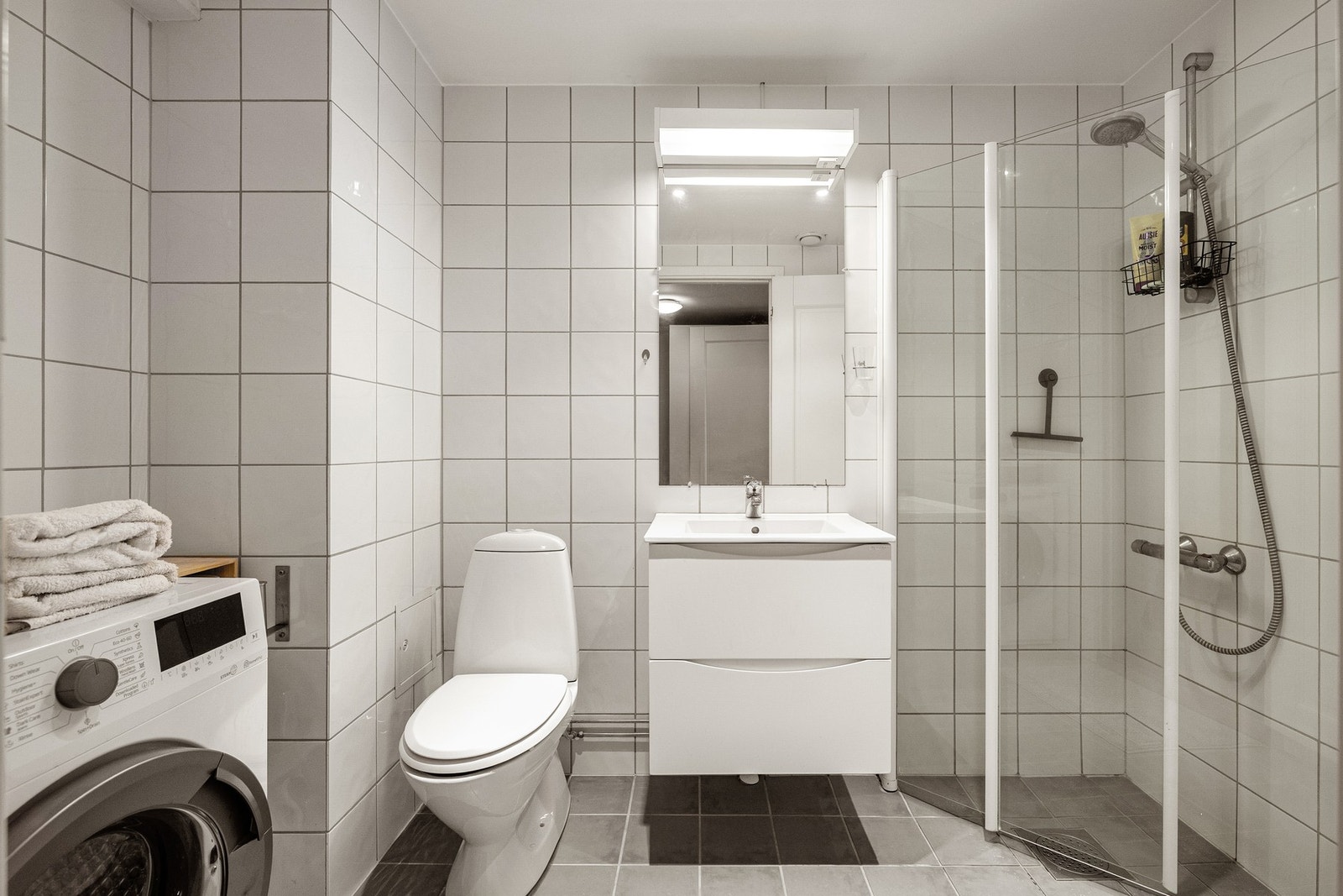 Leiligheten har et lyst og moderne baderom fra 2002. Baderommet har grå fliser på gulv, elektrisk gulvvarme, hvite fliser på veggene og downlights i himlingen. Galleribilde