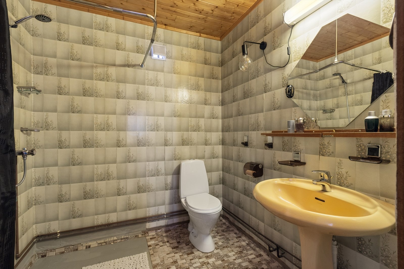 Bad i underetasjen har flislagt gulv med varmekabler, våtromstapet på vegger og panel i taket. Badet er utstyrt med toalett, dusjhjørne med forheng og søyleservant. Galleribilde