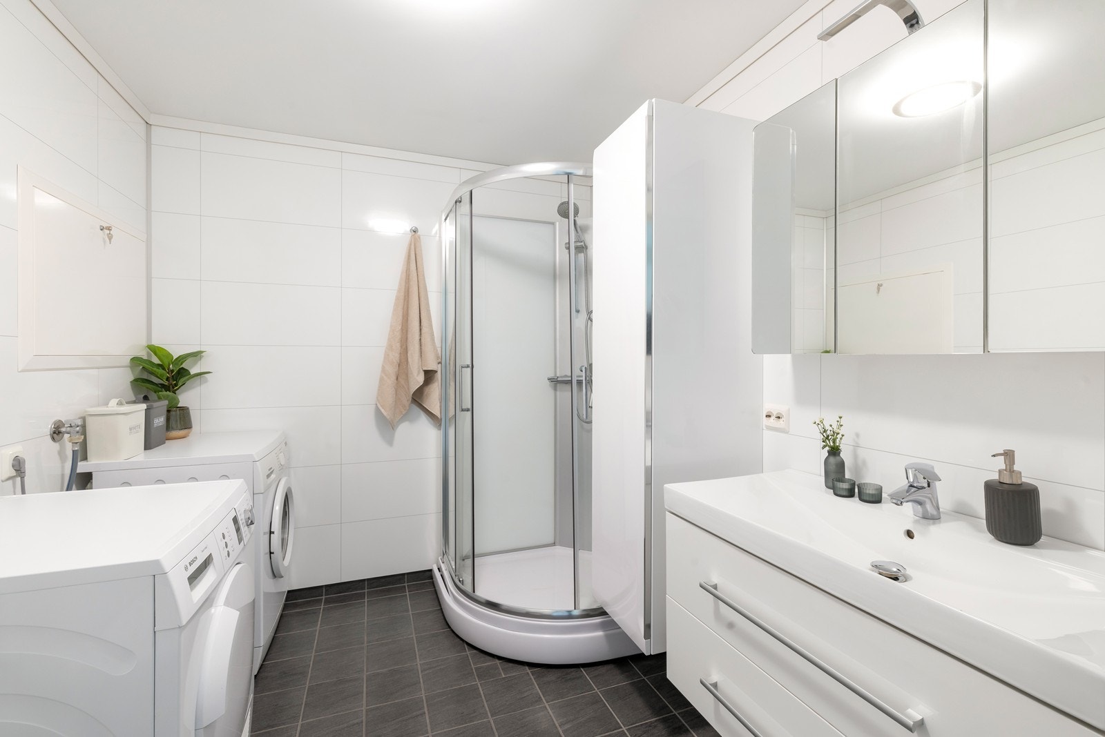 Badet er effektivt innredet med fliser på gulv og innredning bestående av servant med skap og speil, wc og dusjkabinett. Galleribilde