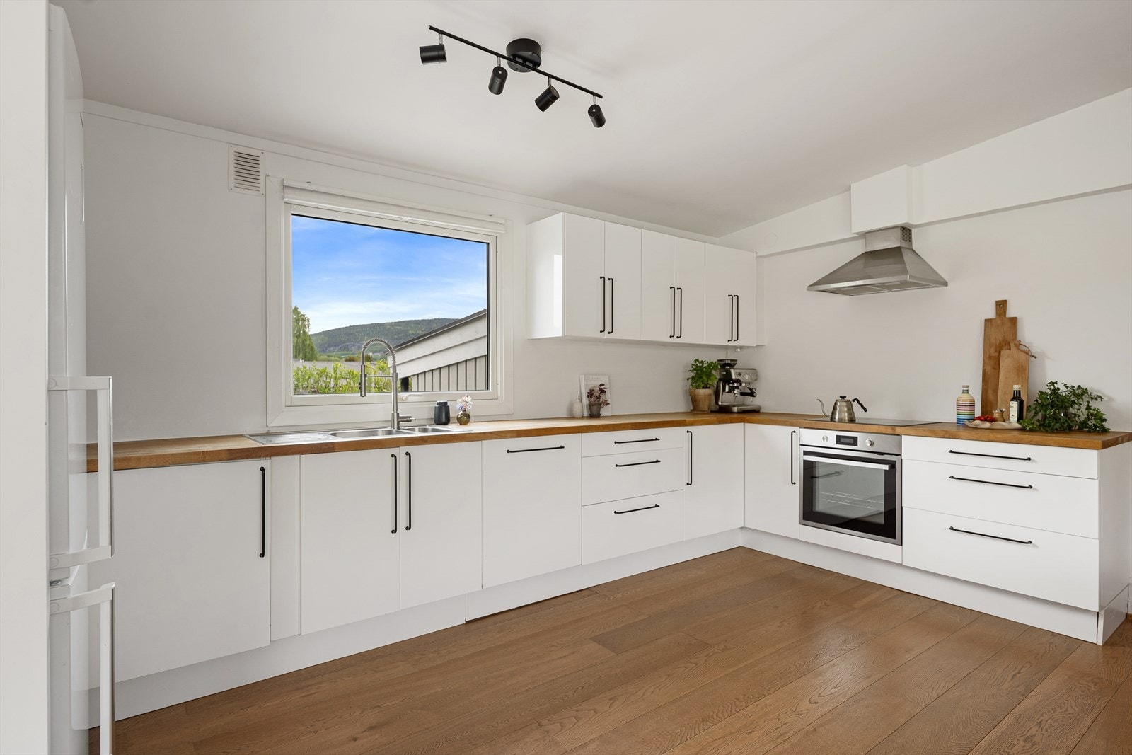 Kjøkkeninnredning med lyse glatte fronter, benkeplater av heltre og malt backsplash. Integrert platetopp, komfyr og oppvaskmaskin. Plass til frittstående kjøl/frys Galleribilde