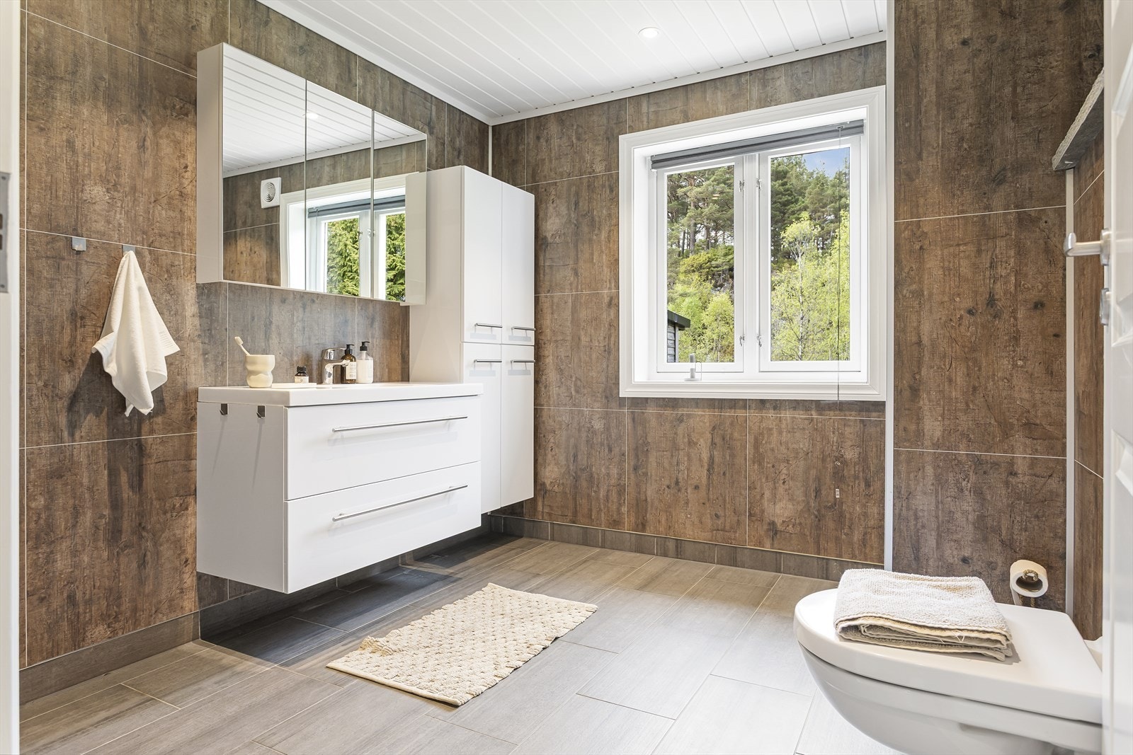 Badet har keramiske fliser på gulv, baderomsplater på veggene og malt panel i himling med innfelte spotlights. Galleribilde