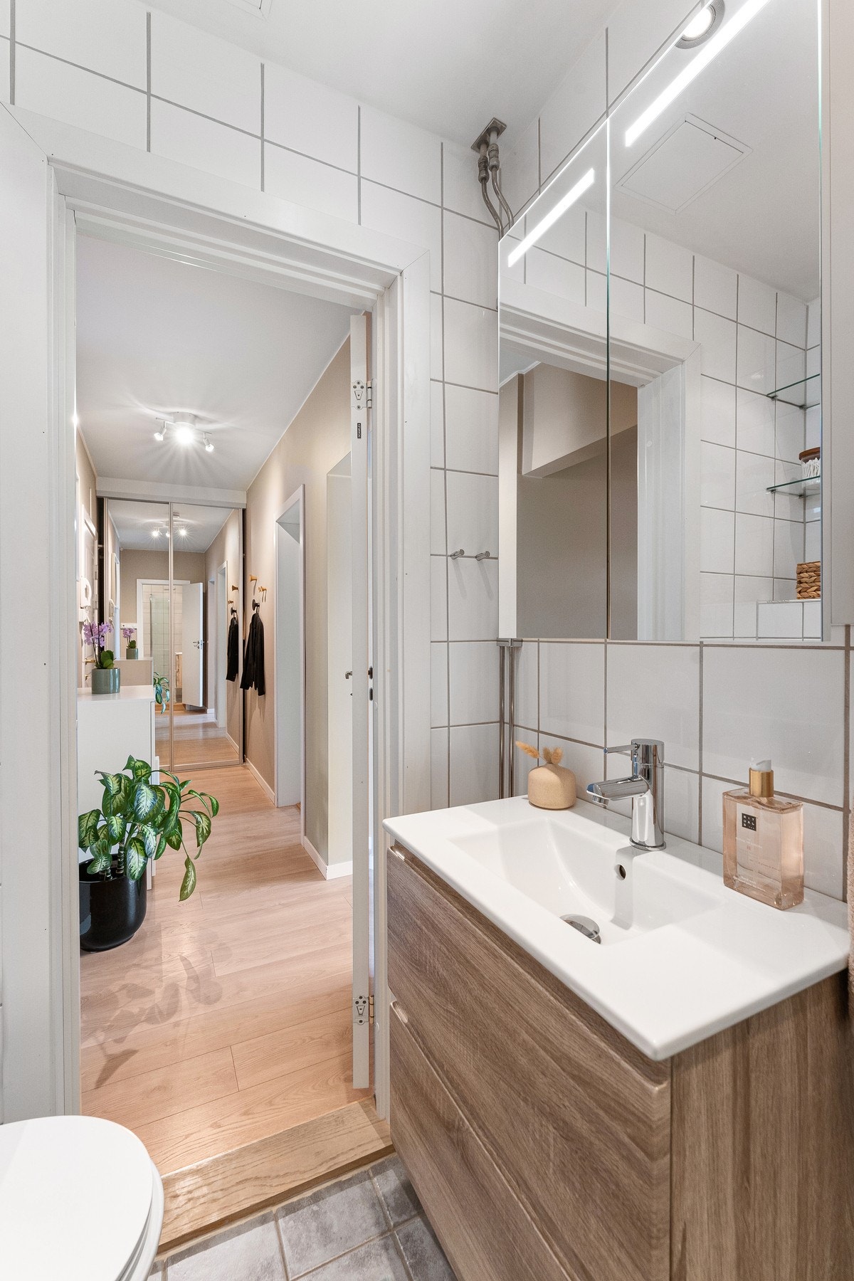 Badet er utstyrt med dusjhjørne med svingdører i glass og regnfallsdusj. God oppbevaringsplass i stort servantskap med heldekkende servant. Veggmontert klosett og opplegg for vaskemaskin Galleribilde