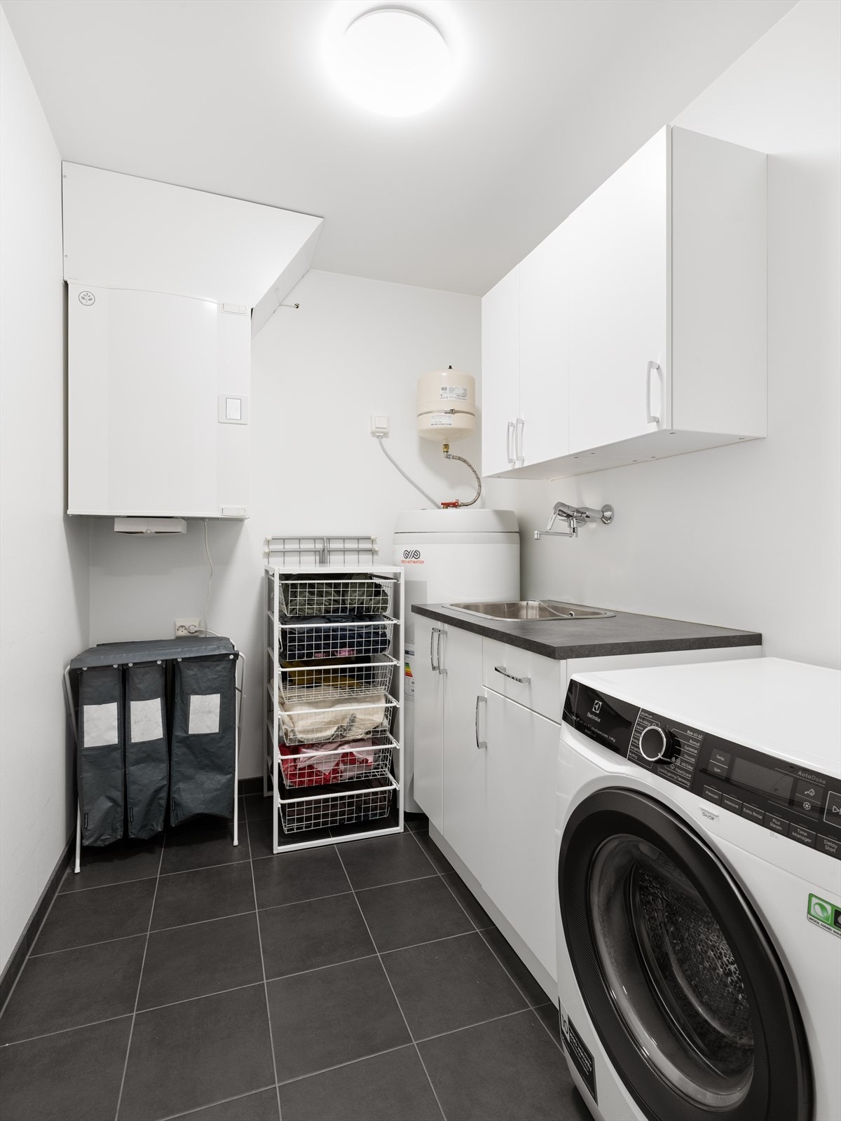 Separat vaskerom med flislagt gulv med varmekabler, opplegg for vaskemaskin og plassering av ventilasjonsanlegg og varmtvannsbereder. Galleribilde