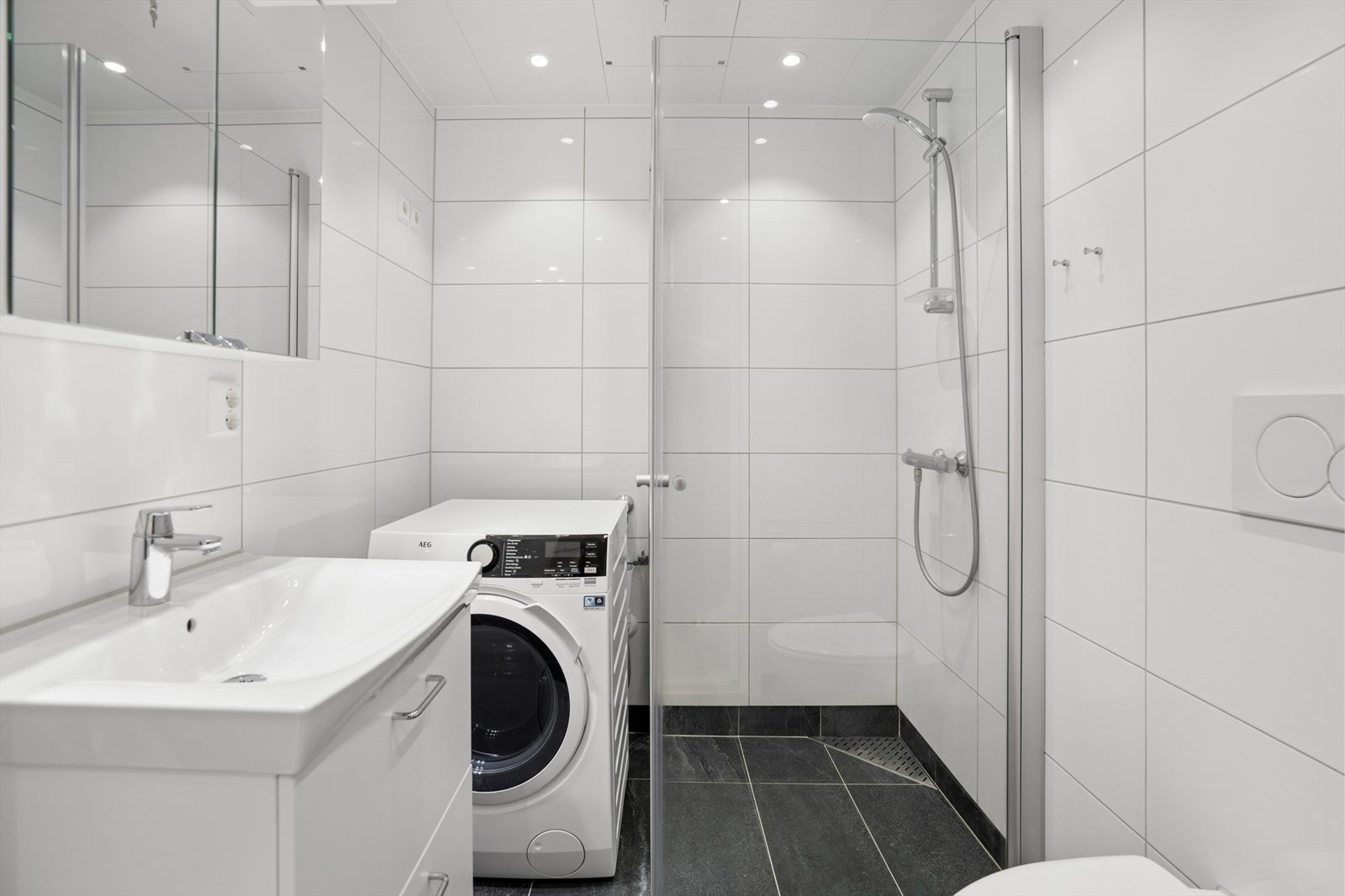Baderom har også stilren innredning med speilskap og servant med skuffer. Det er plass til vaskemaskin i hjørnet av badet. Galleribilde