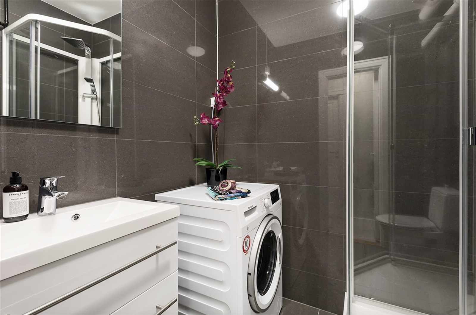 Badet er innredet med usjkabinett, servant med underskuffer samt speil og belysning over servant. Det er gulvmontert toalett og opplegg for vaskemaskin og tørketrommel. Galleribilde