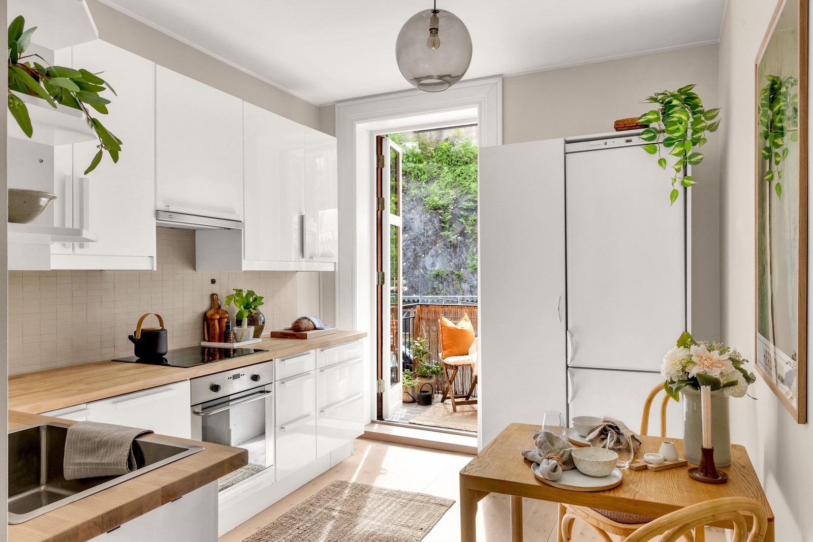 Kjøkkeninnredning med slettmalte fronter utstyrt med benkeplate av tre, stekeovn, platetopp, oppvaskmaskin og frittstående kjøleskap med frysedel. Galleribilde