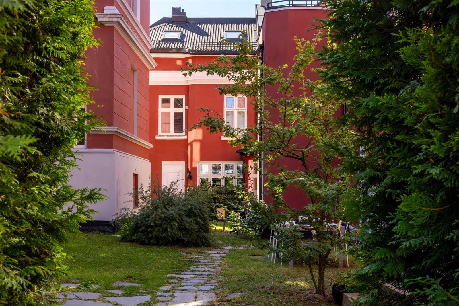 Steinlagte stier slynger seg gjennom det grønne uterommet, mens trær, hekker og blomstrende vekster gir tomten et innbydende og privat preg. Galleribilde