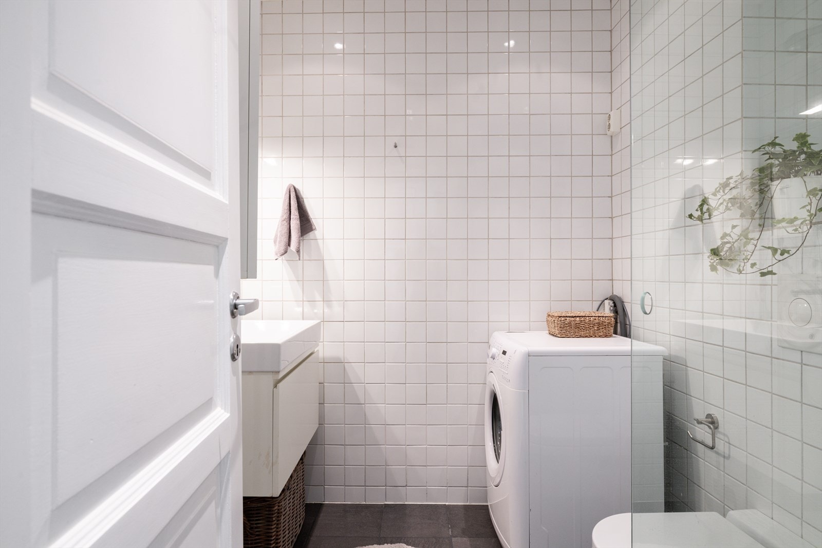 Delikat og lyst bad innredet i moderne stil. Badet er utstyrt med dusjhjørne, praktiske oppbevaringsløsninger og opplegg for vaskemaskin Galleribilde