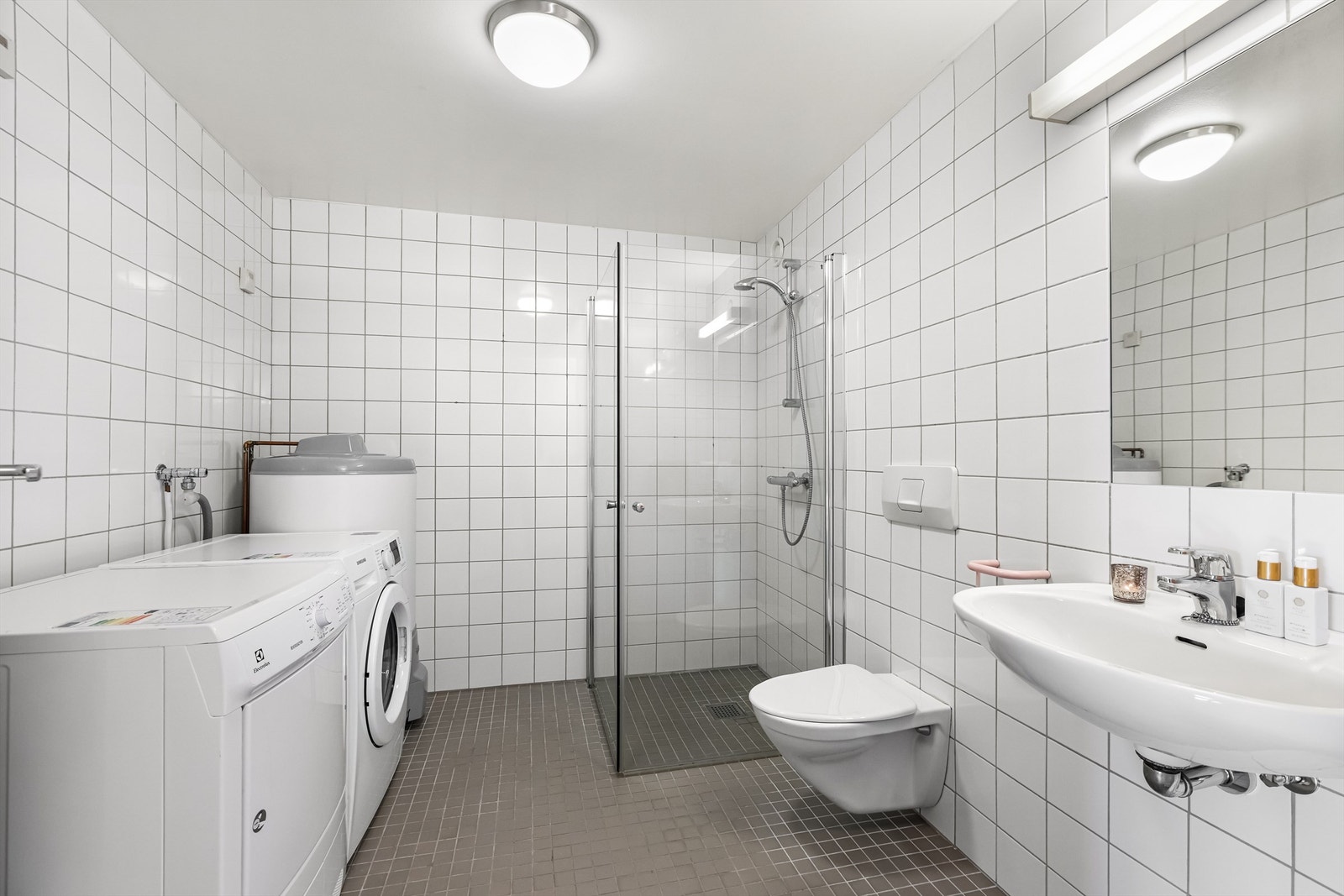 Flislagt bad med elektrisk gulvvarme, dusjhjørne, vegghengt toalett og opplegg for vaskemaskin. Galleribilde