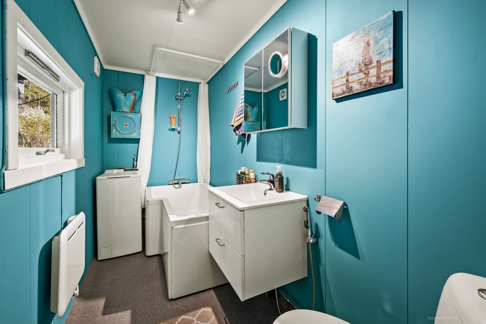 Badet har malte baderomsplater på veggene og er utstyrt med badekar, servant og toalett. Galleribilde