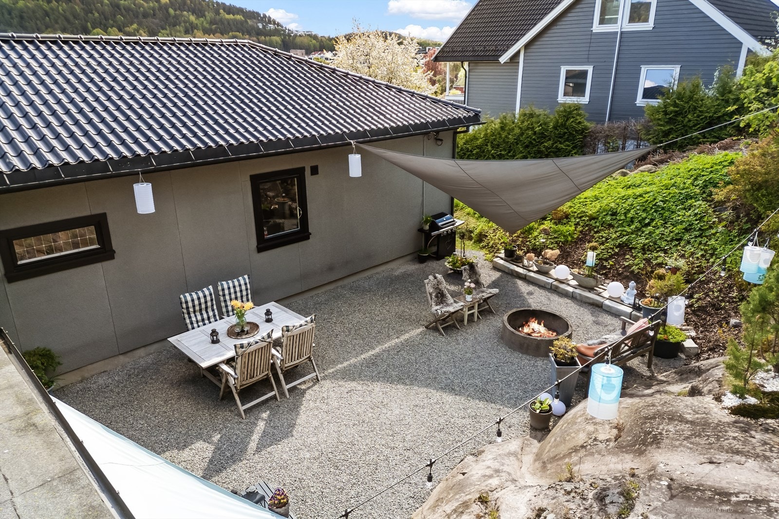 Tomten er opparbeidet med en lettstelt, gruset uteplass og ligger i et skrånende terreng med skogen som nærmeste nabo. Galleribilde
