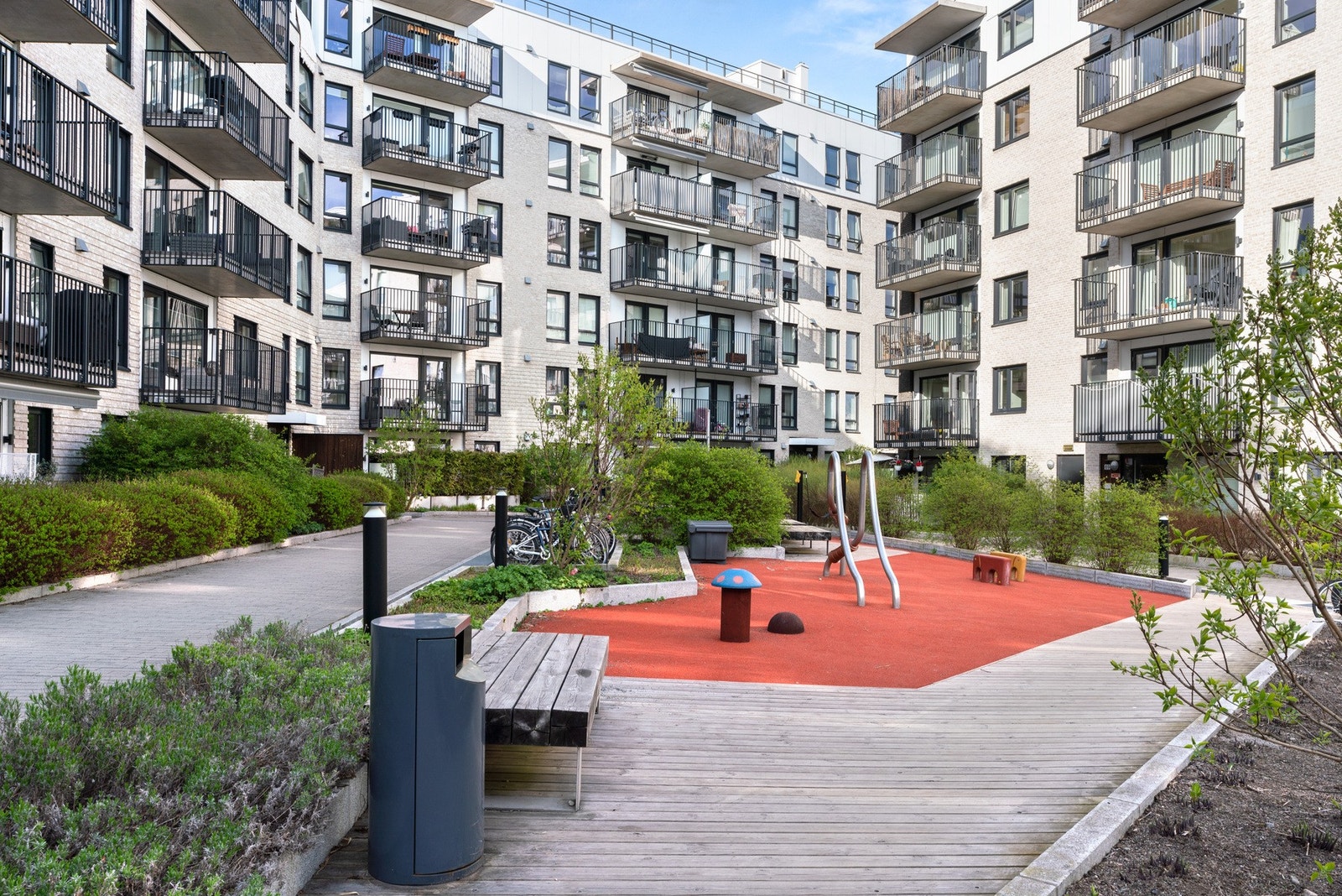 Pent opparbeidet gårdstun med steinsatte gangveier, sykkelstativer, beplantning, faste benker og lekeplass med mykt dekke. Galleribilde