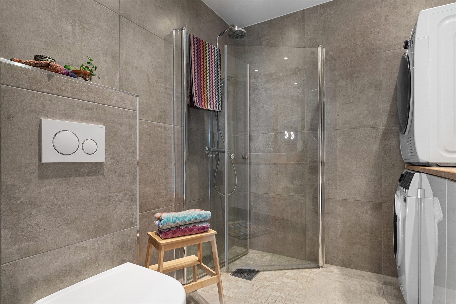 Badet er også innredet med vegghengt toalett og dusjhjørne med innfellbare glassvegger, hånd- og regnfallsdusj. Det er i tillegg opplegg til vaskemaskin. Galleribilde