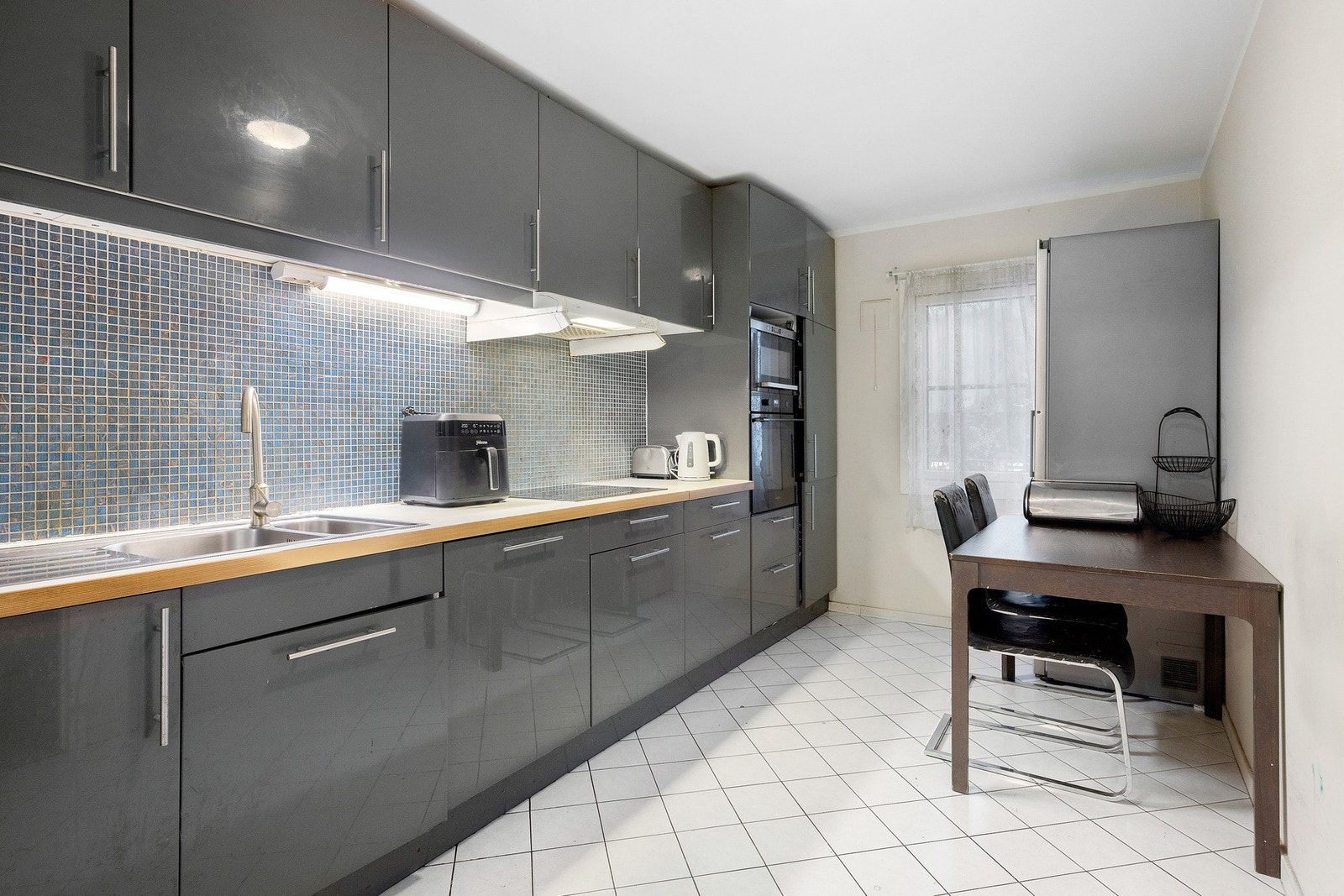 Pent kjøkken med mørke, grå høyglansfronter, mosaikk-flislagt backsplash i blå og grå nyanser Galleribilde