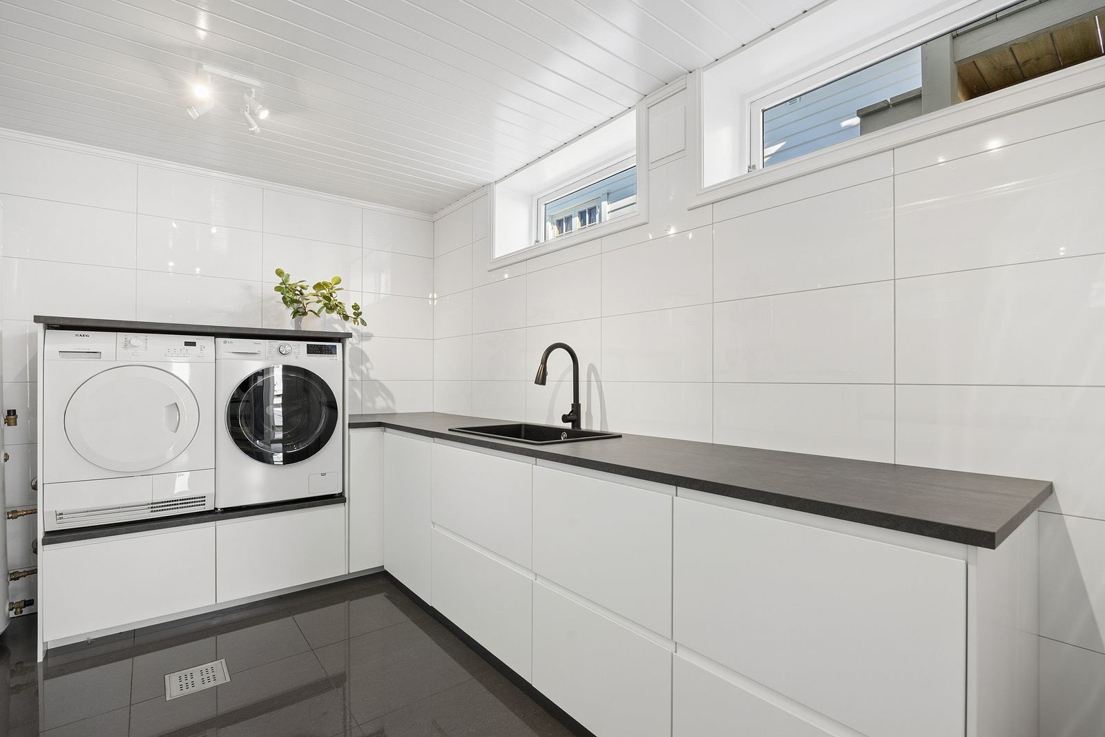 Eget vaskerom med flislagt gulv og praktisk innredning. Her er det opplegg for vaskemaskin, vask i benk, en svært funksjonell del av boligen. Galleribilde