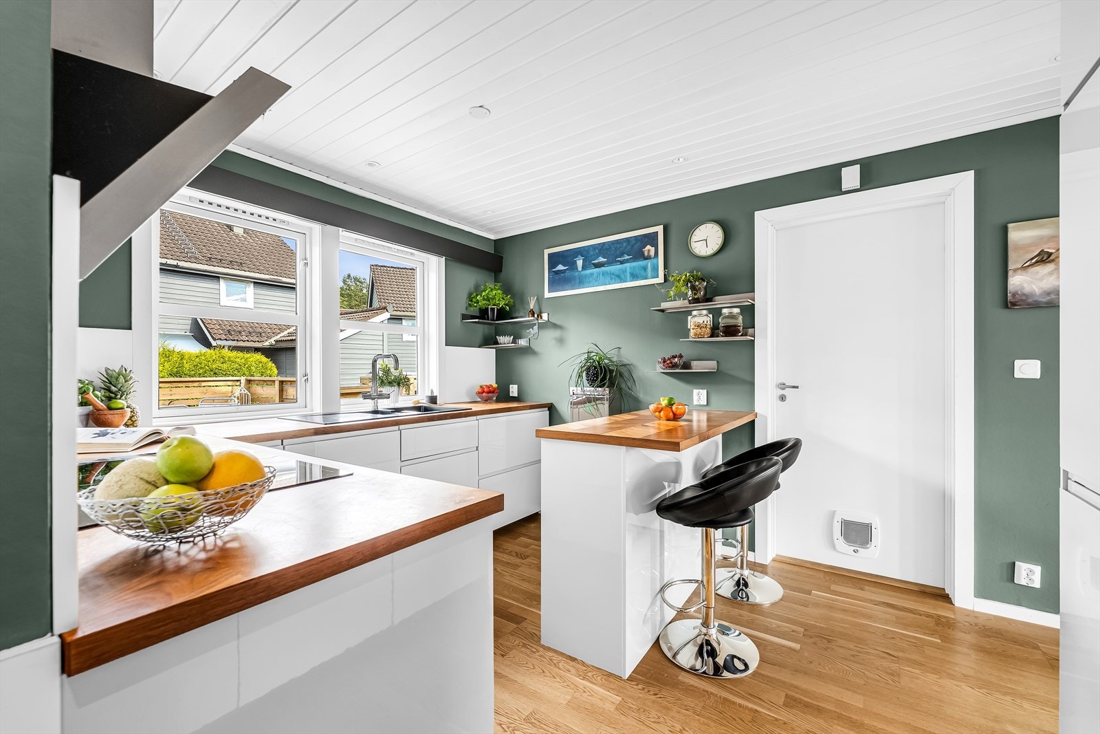 Kjøkken med slette fronter i åpen løsning mot deler av stuen. Nedfelt komposittkum i laminert benkeplate. Integrerte hvitevarer bestående av koketopp, stekeovn, mikrobølgeovn, kjøl-/fryseskap og oppvaskmaskin. Galleribilde