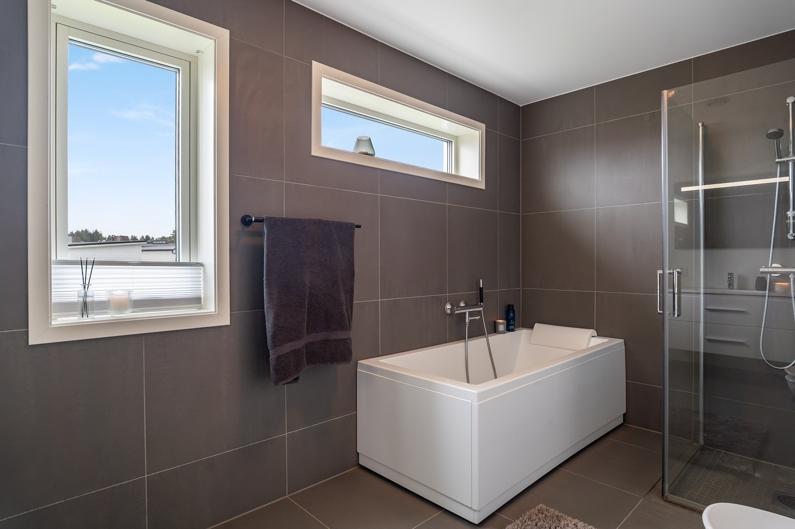 Badet er innredet med dusjhjørne som har to glassdører, badekar med hånddusj, hvit baderomsinnredning og speil med belysning. Galleribilde
