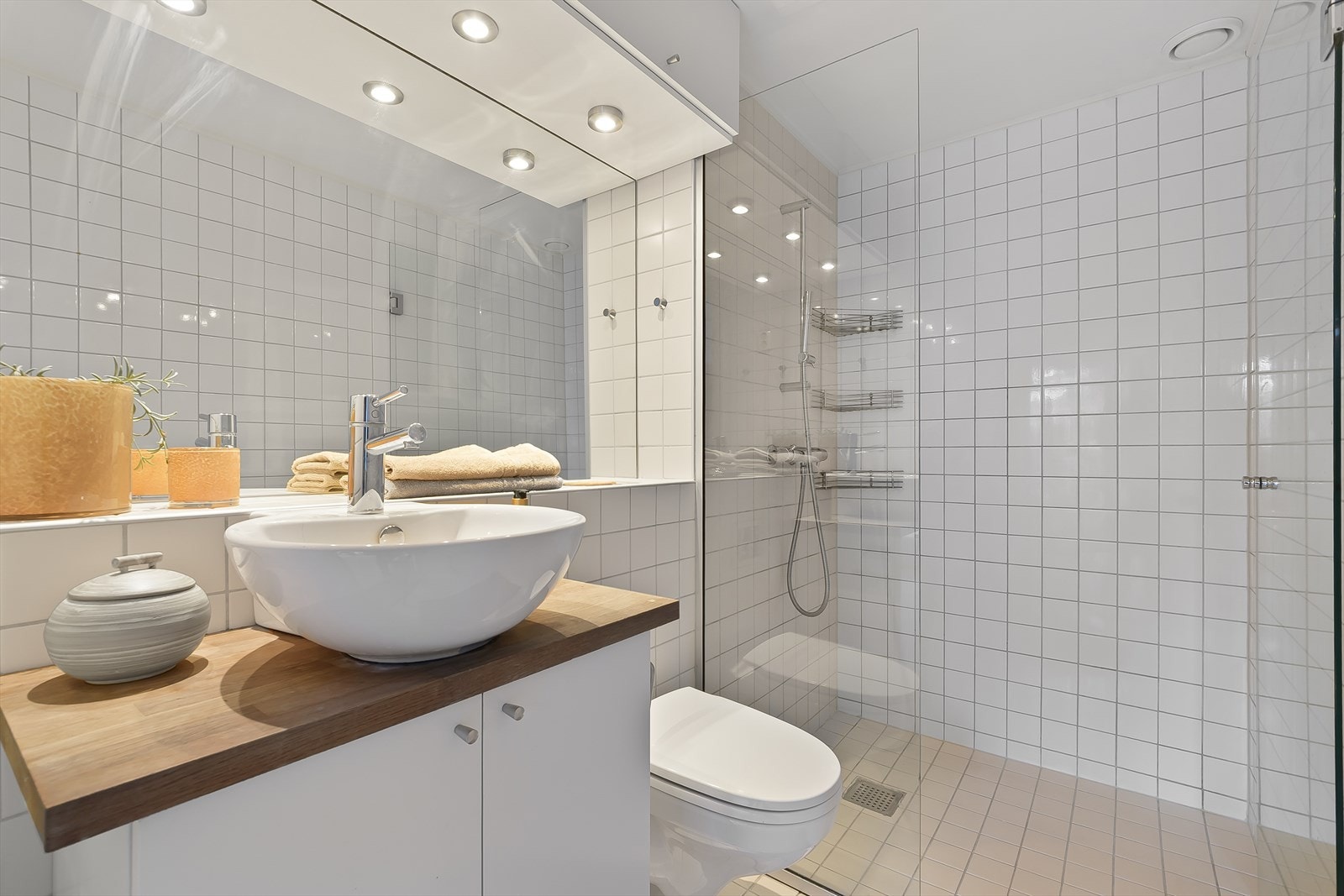 Pent, flislagt bad innredet med dusjnisje med glass vegger, veggmontert toalett og innredning med servant over benkeplate med speil. Galleribilde