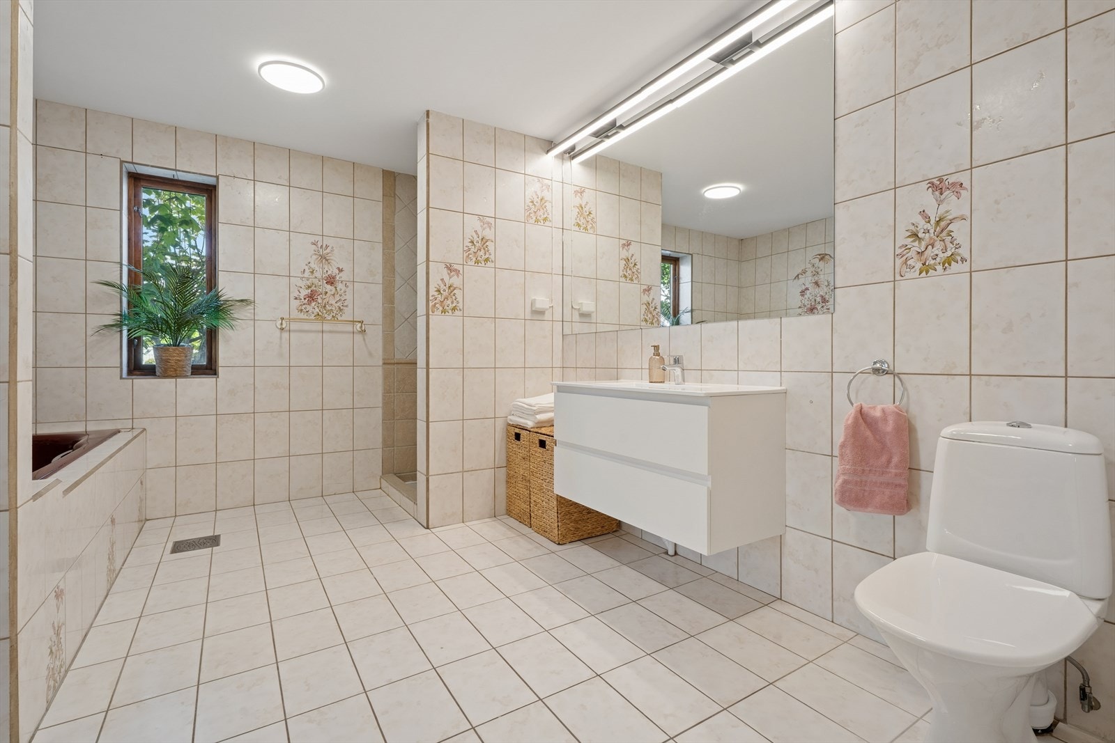 Badet i 1. etasje er flislagt og fra byggeår. Det inneholder innmurt badekar, toalett og et skjermet dusjhjørne. Servanten har tilhørende speil på vegg. Galleribilde