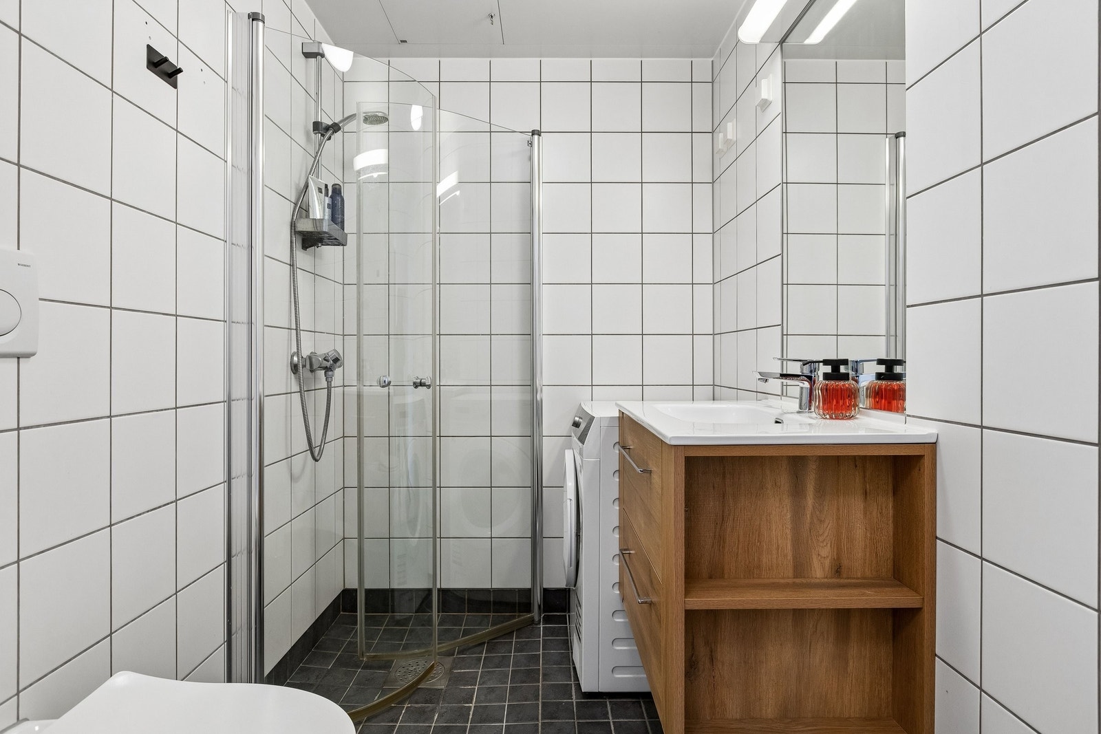 Flislagt bad med baderomsinnredning og vegghengt speil med belysning over speilet. Galleribilde