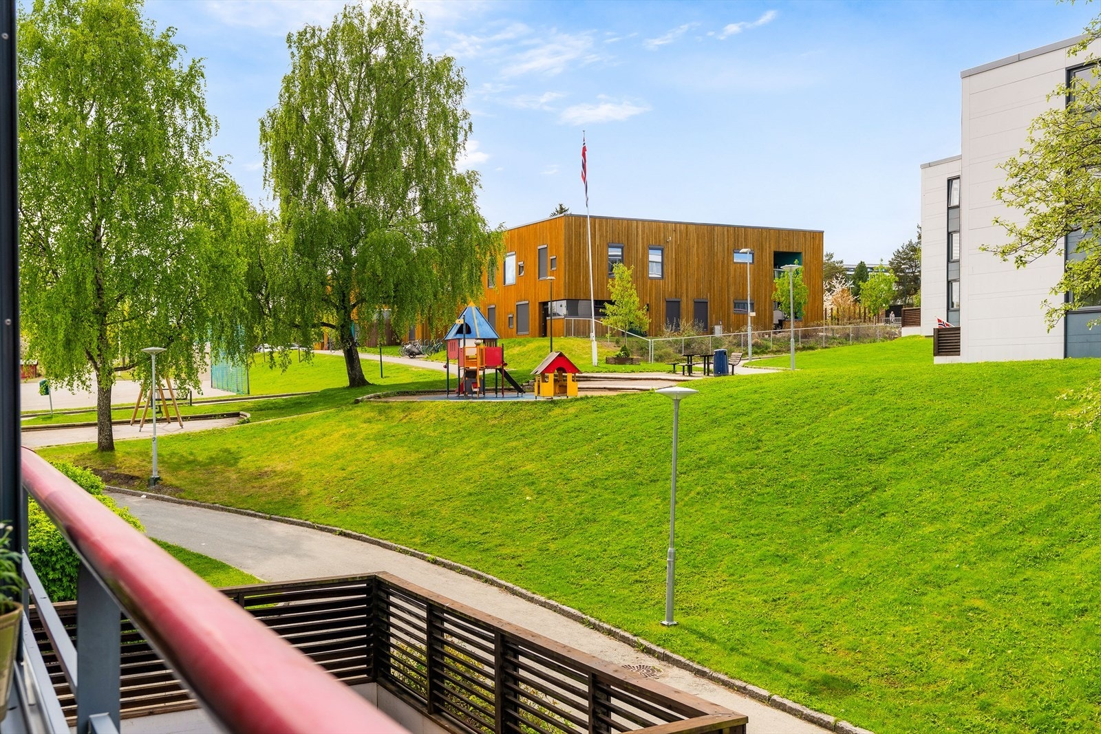 Balkongen vender ut mot borettslagets grønne fellesområde med lekeplass og sittebenker. Galleribilde