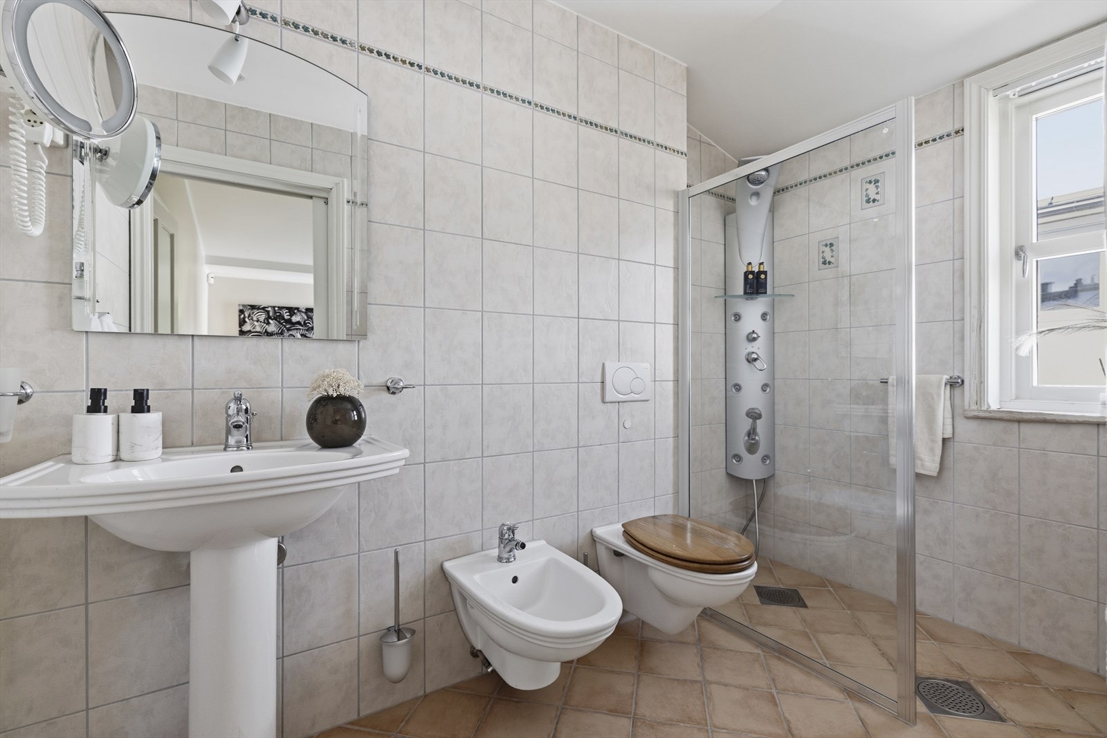 Dusjhjørne med dusjarmatur og dusjvegg. Veggmontert toalett, bidet og servant med blandebatteri Galleribilde