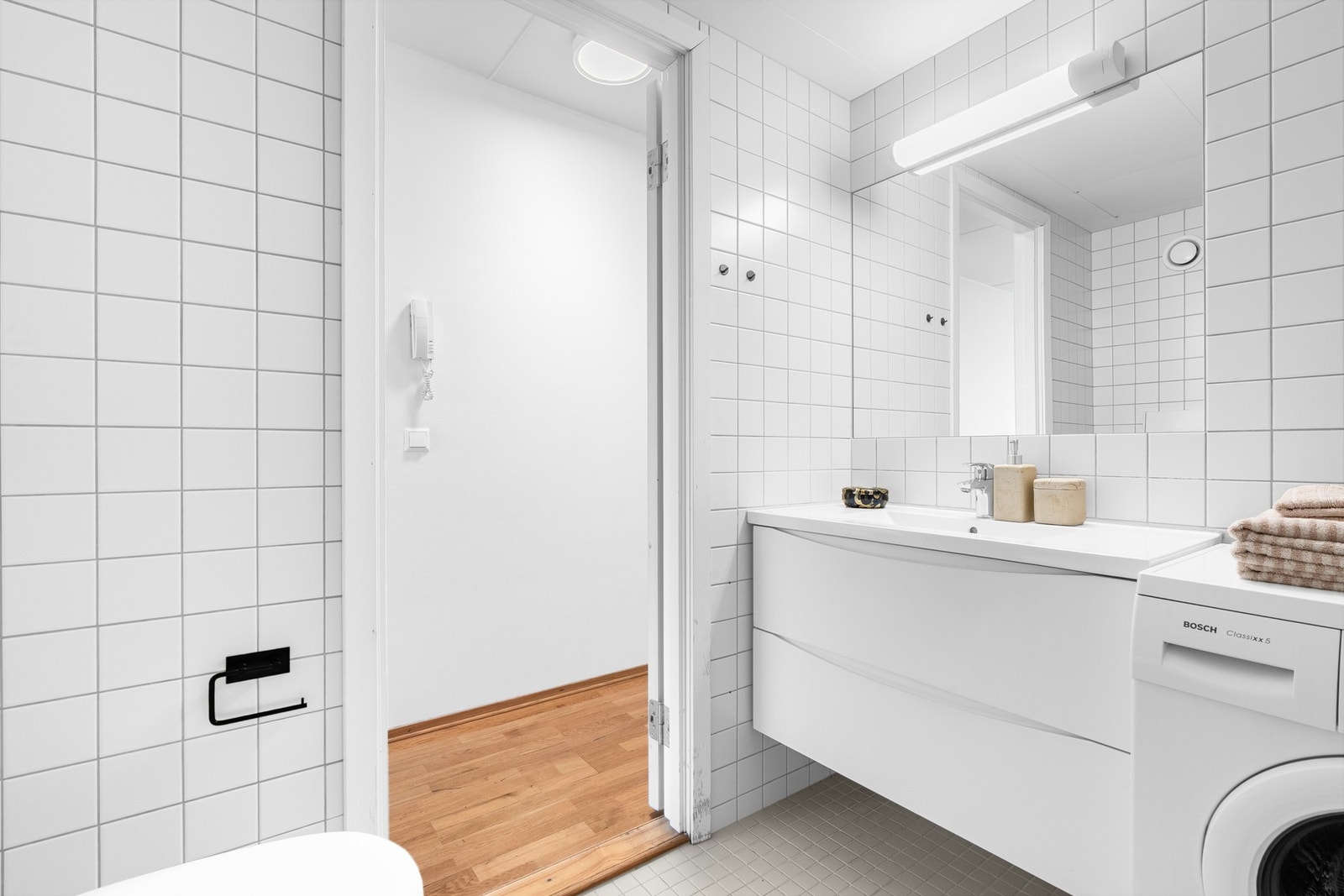 Moderne baderomsinnredning med skuffer og heldekkende servant, speil med belysning over. I hjørnet er det plass og opplegg for vaskemaskin. Galleribilde