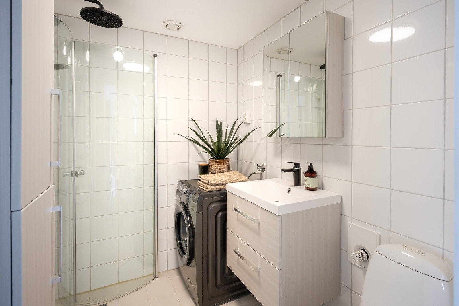 Stilrent baderom med flis på gulv og vegger. Badet er praktisk utformet med innfellbare dusjdører som gir mer gulvplass når dusjen ikke er i bruk. Galleribilde