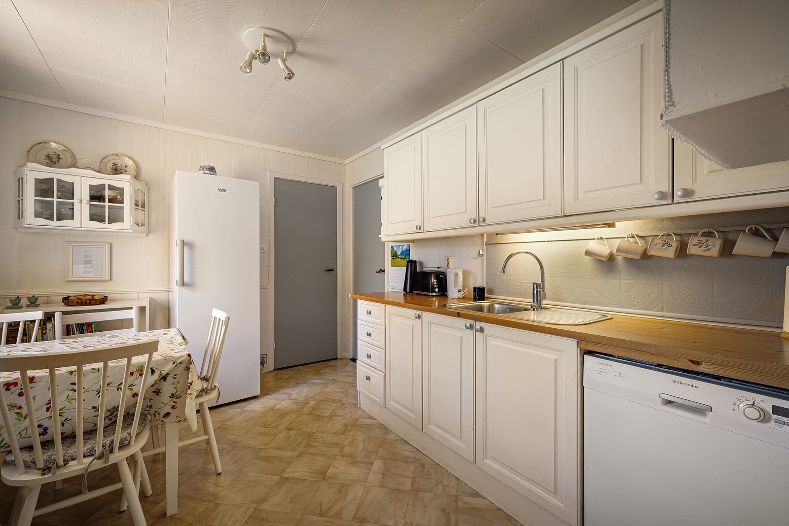 Kjøkken med innredning av malte trefronter og laminat benkeplate. Kjøkkenet er utstyrt med integrert komfyr og ventilator, samt frittstående kjøleskap. Det er opplegg for oppvaskmaskin. Galleribilde
