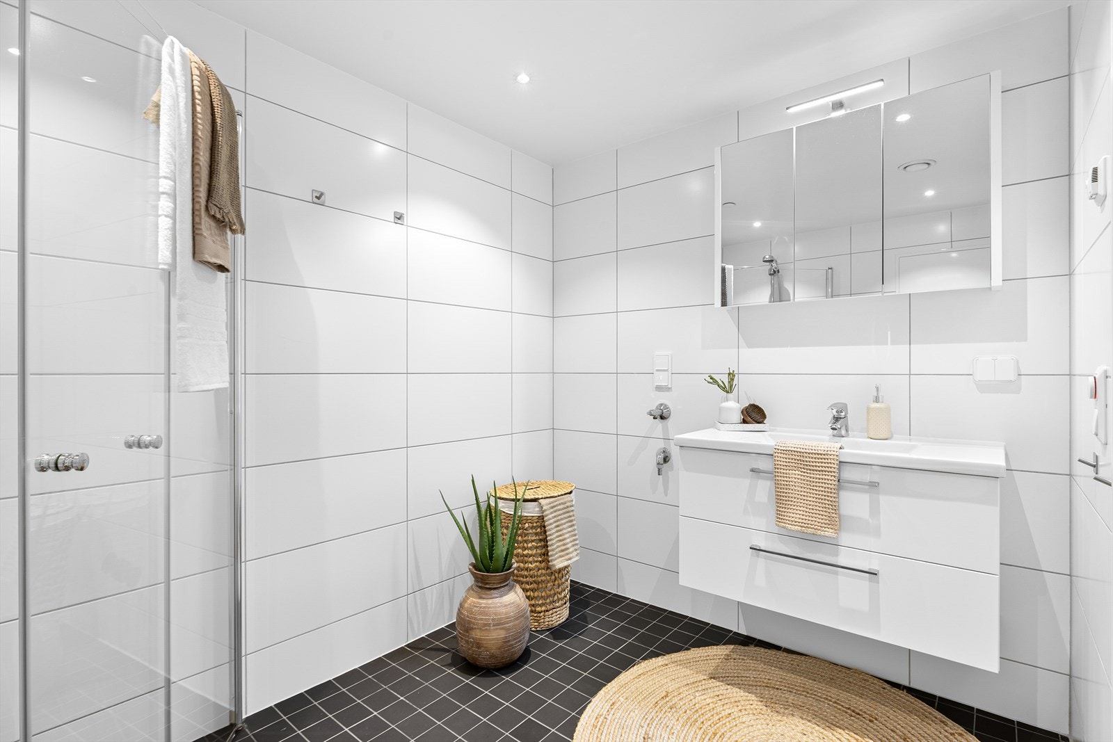 Badet er funksjonelt utstyrt med dusjhjørne med innfellbare dører, servant i skap, veggmontert toalett og opplegg for vaskemaskin. Galleribilde