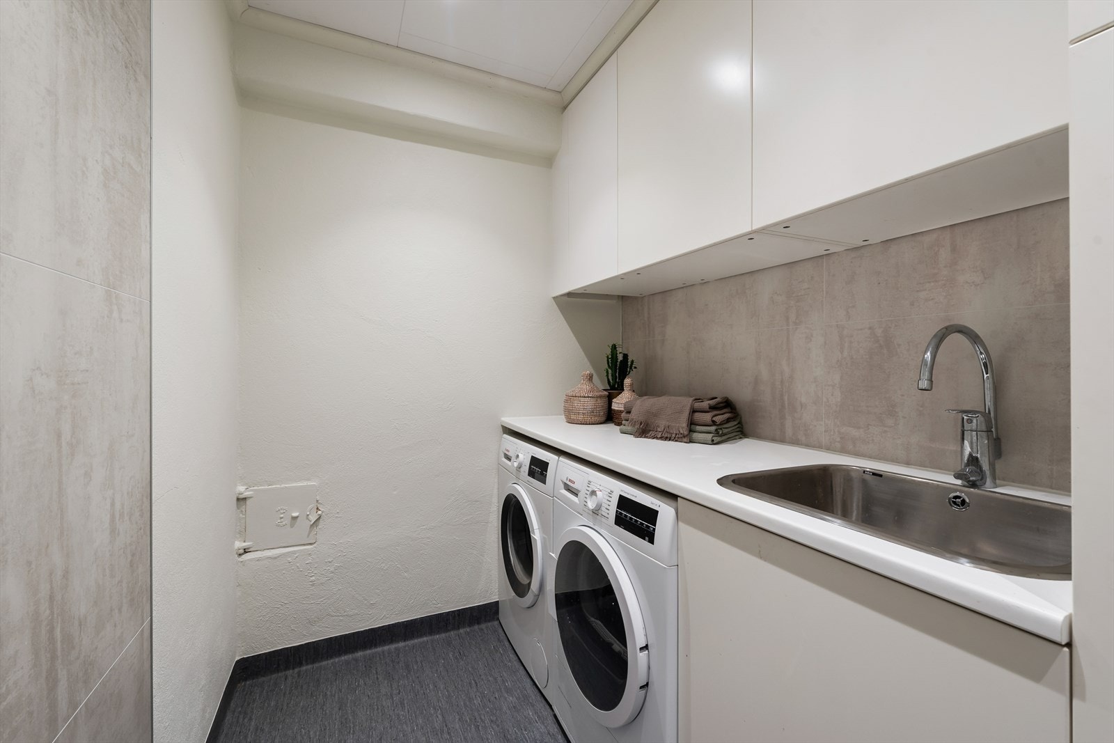Med inngang fra badet er et svært praktisk vaskerom med opplegg for vaskemaskin og tørketrommel, utslagsvask, benkeplate og overskap. Galleribilde