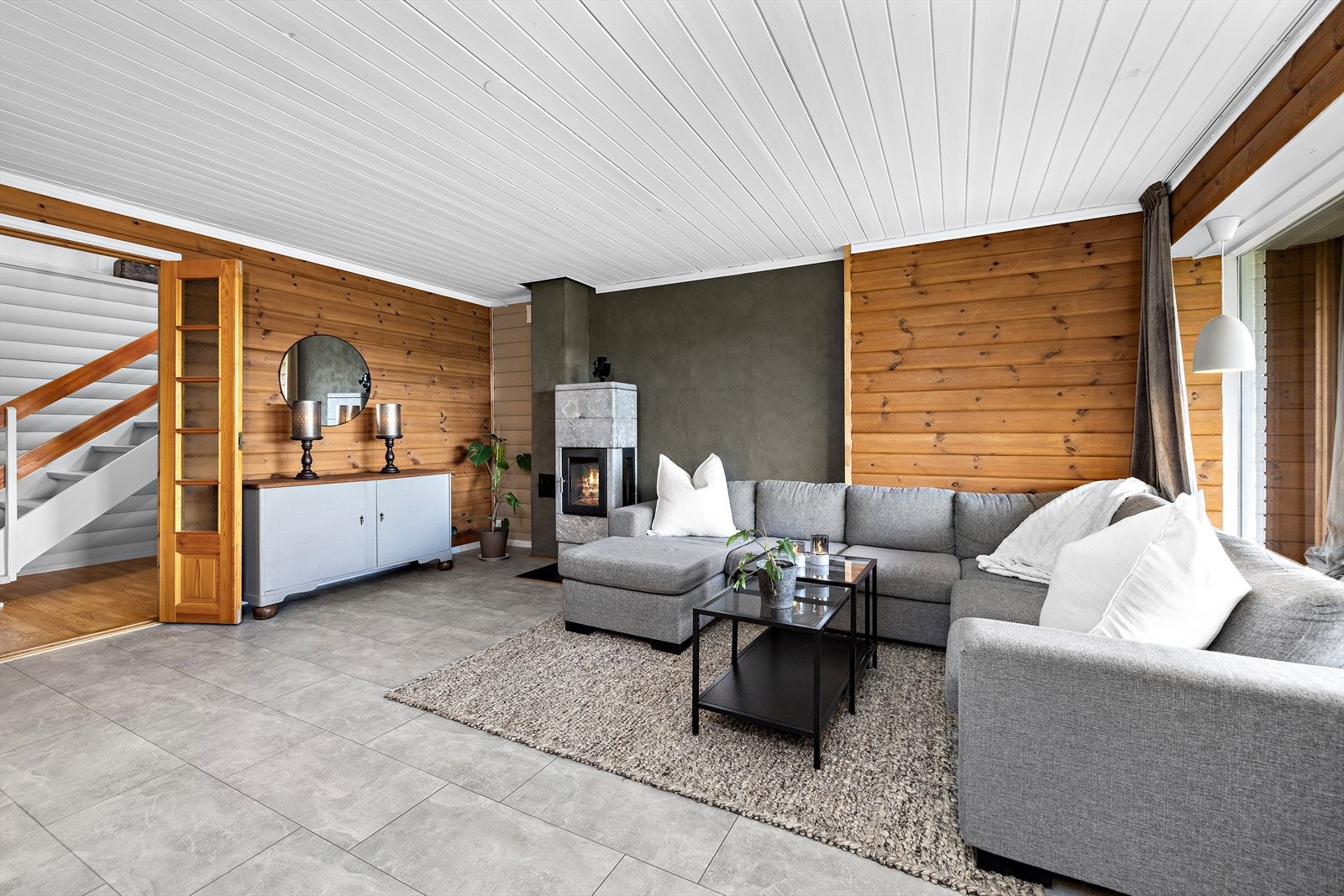 Stuen er lun og koselig med fliser på gulvet, panelvegger og pipeløp. Galleribilde