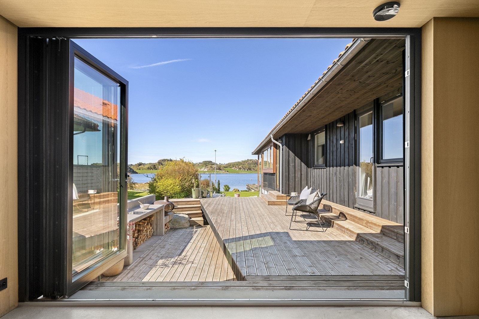 Store foldedører åpner opp mot uteområdet og skaper en sømløs overgang mellom inne- og utearealene. Her sitter man helt privat, allikevel med utsikt og nærhet til fjorden. Galleribilde