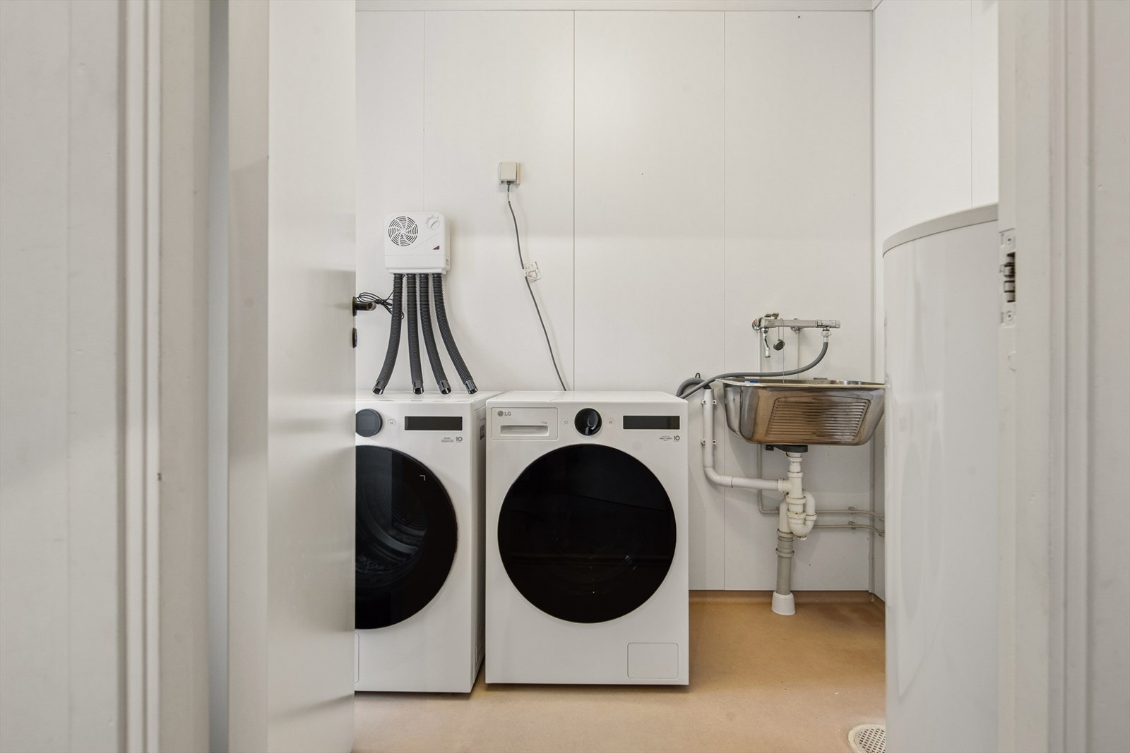 Praktisk vaskerom med opplegg for vaskemaskin, utslagsvask og nyere varmtvannsbereder. Galleribilde