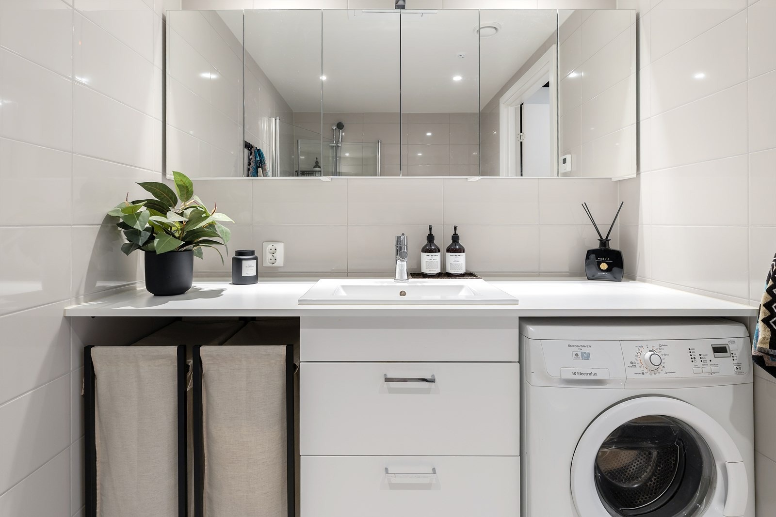 Badet er videre innredet med smarte oppbevaringsløsninger bestående av benkeskap og speilskap. Vaskemaskin er praktisk plassert under benkeplate, som gir ekstra arbeidsflate og bidrar til en funksjonell og ryddig utnyttelse av rommet. Galleribilde