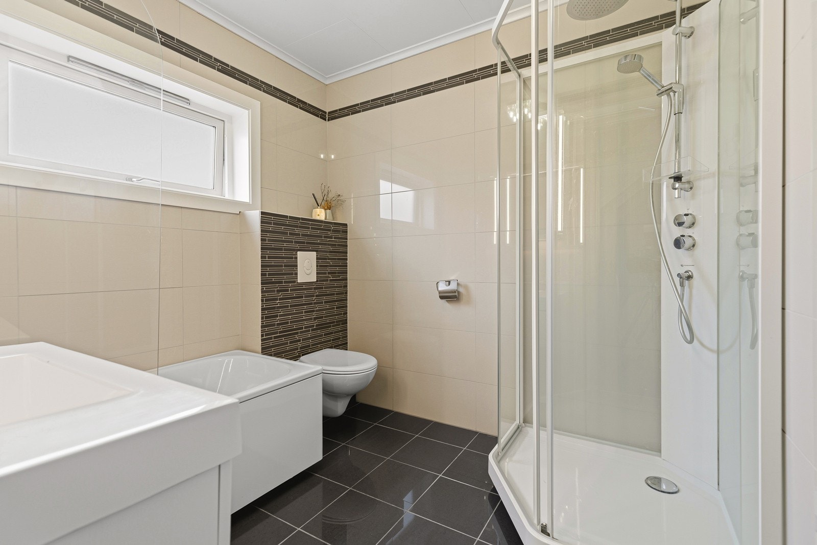 Badet er flislagt og utstyrt med både dusjkabinett, badekar og vegghengt toalett Galleribilde