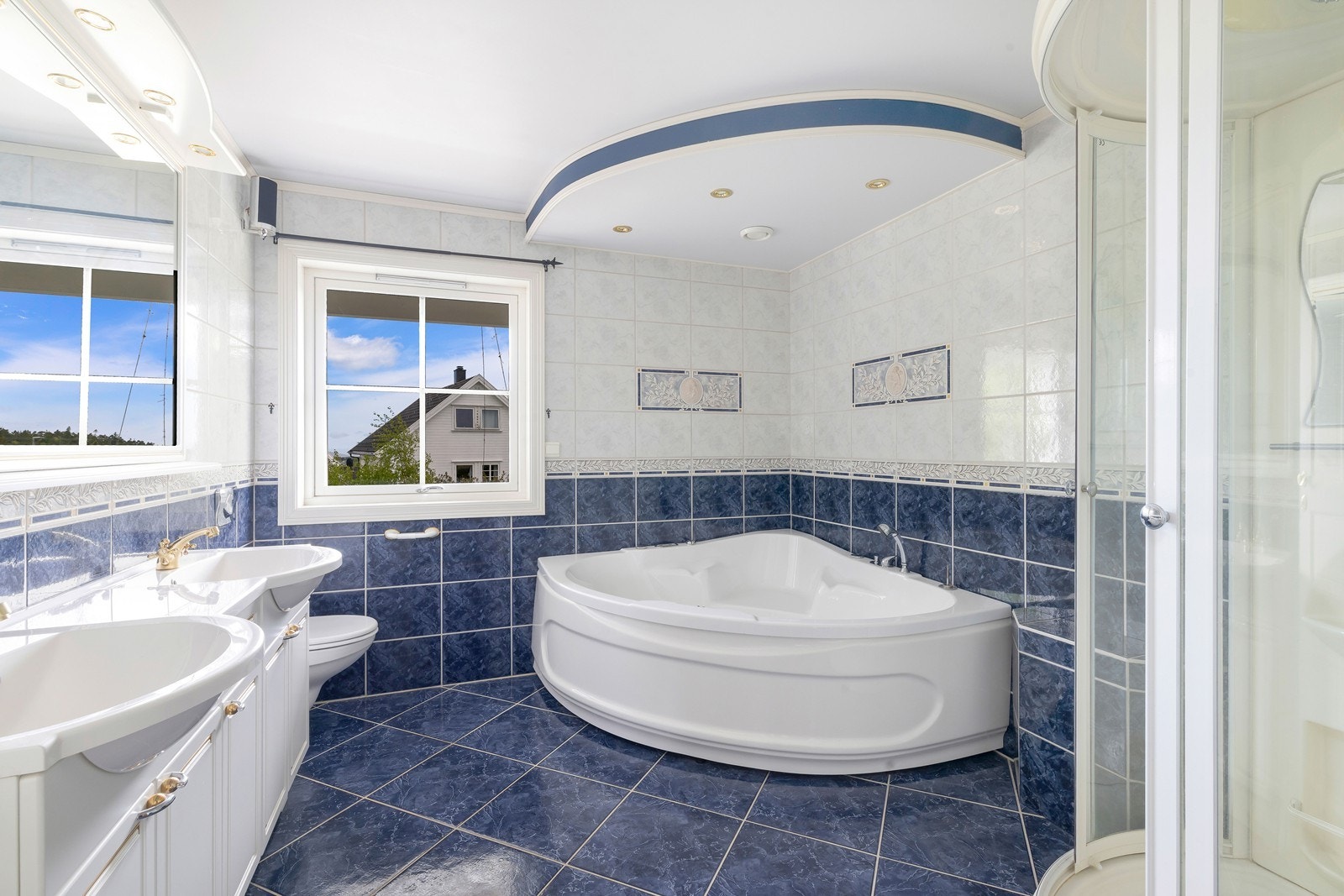 Badet er flislagt med varme i gulv, innredet med dusj , hjørnekar, dobbel servant og toalett. Galleribilde
