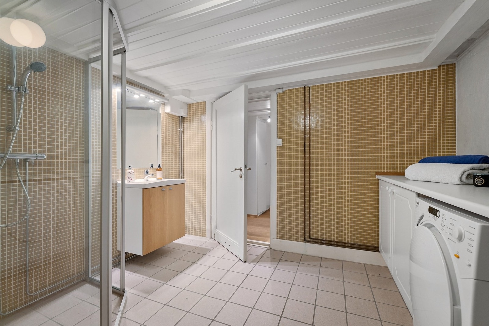 Bad 3/vaskerom (u-etasje) - Badet har mosaikkfliser og pussede murvegger på vegger, samt malt panel i himling. På gulvet er det fliser med varmekabler. Rommet er innredet med baderomsinnredning med nedfelt servant, innfliset speil, dusjhjørne med skyvedør Galleribilde