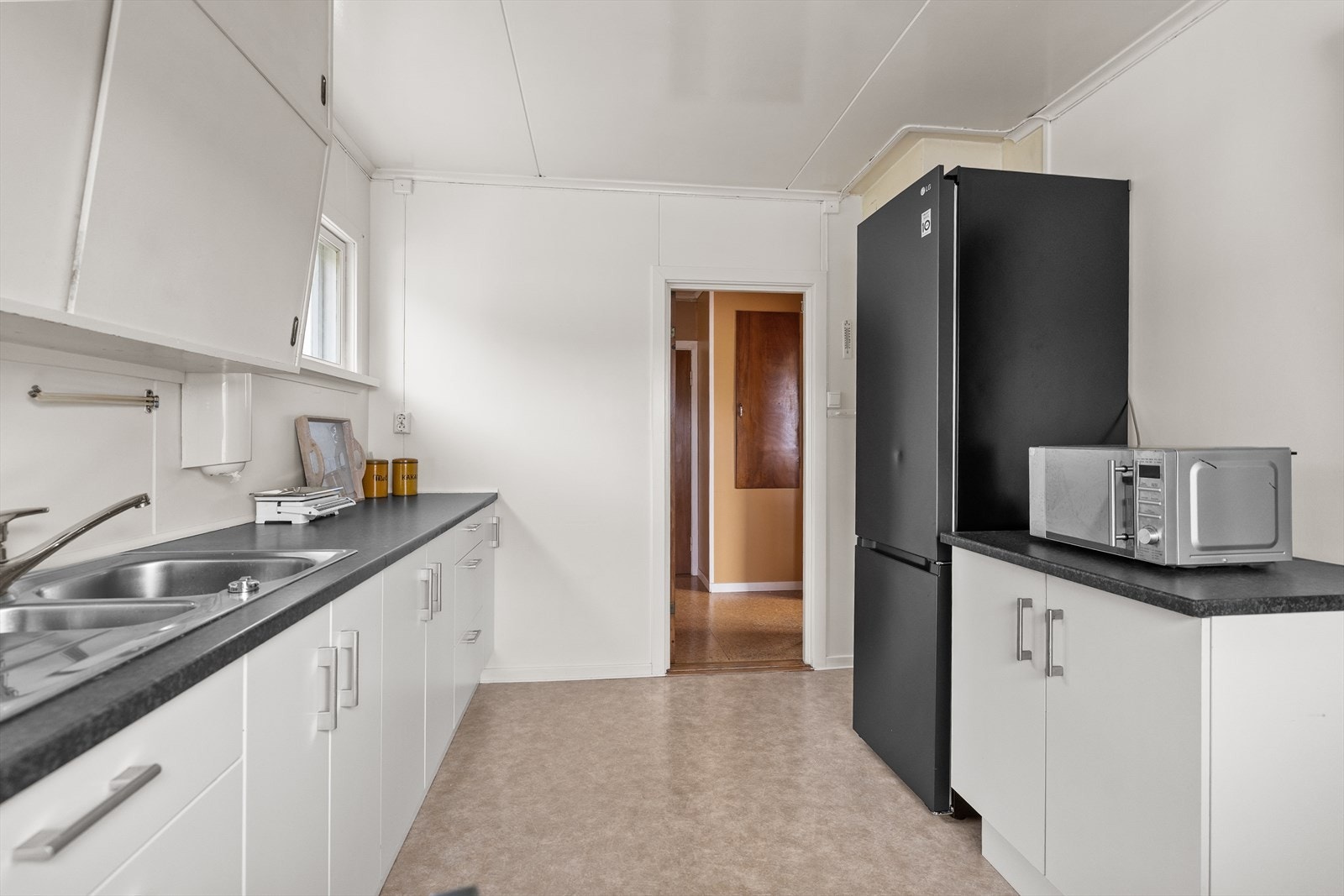 Kjøkken med eldre innredning bestående av glatte fronter og laminert benkeplate med nedfelt rustfri kum og beslag. Galleribilde