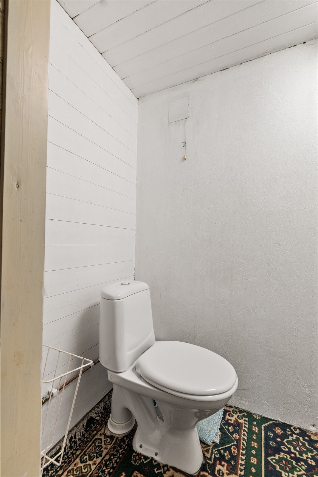 Toalettrommet har betonggulv og teppe, vegger i malt mur og malt kledning, og tak med malte bord. Innredet med klosett. Galleribilde
