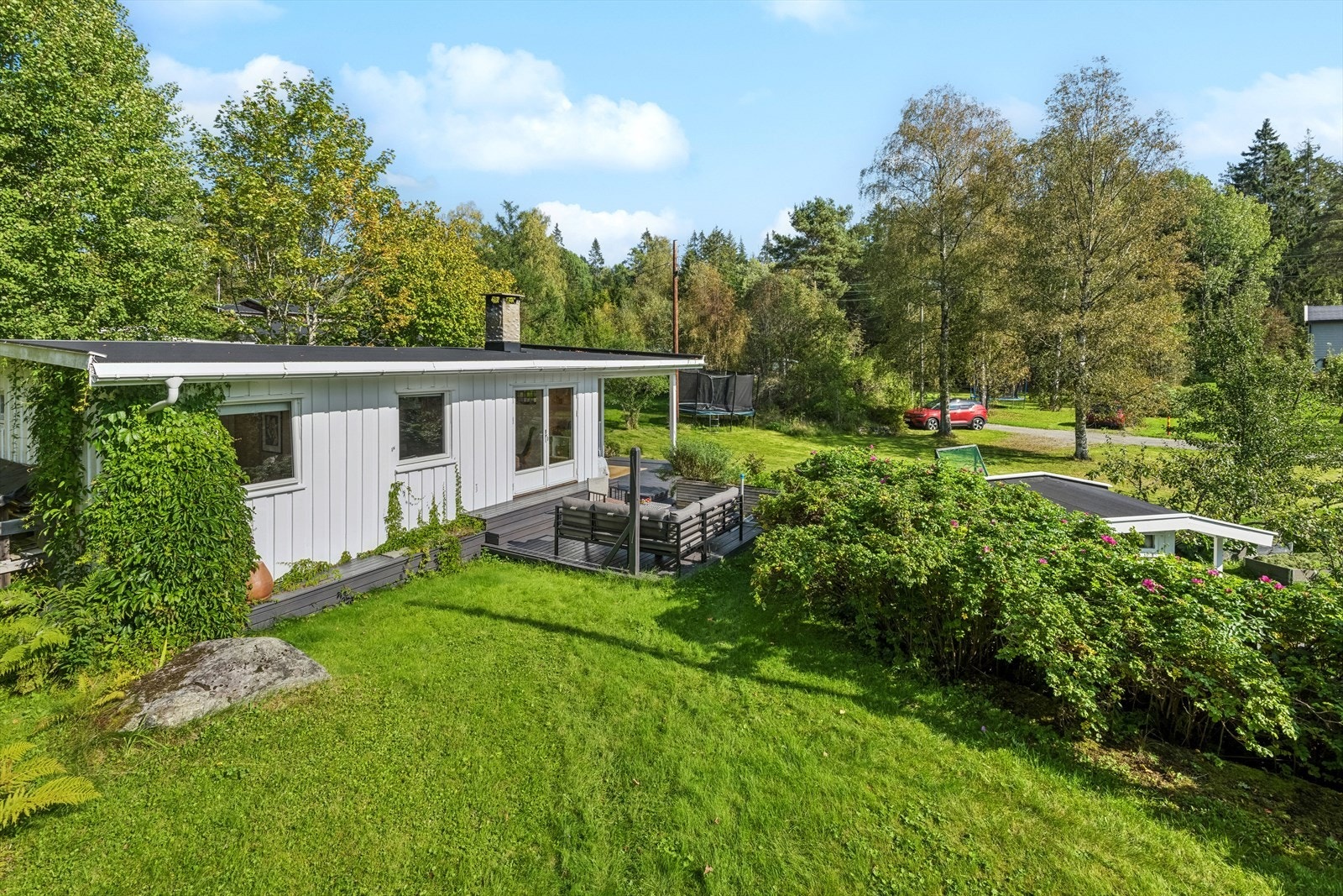 Eiendommen ligger på en pent opparbeidet eiertomt med gressplen, frukttrær og synlig fjell. Galleribilde